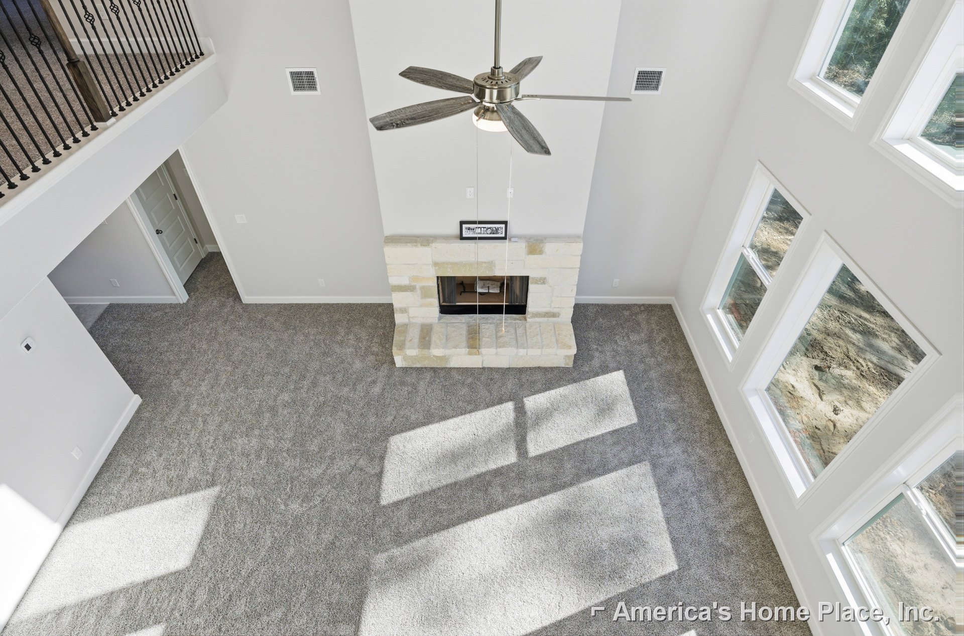 Ceiling fan with integrated light fixture mounted on white ceiling above living room with metal staircase railing, wall vent, and window.