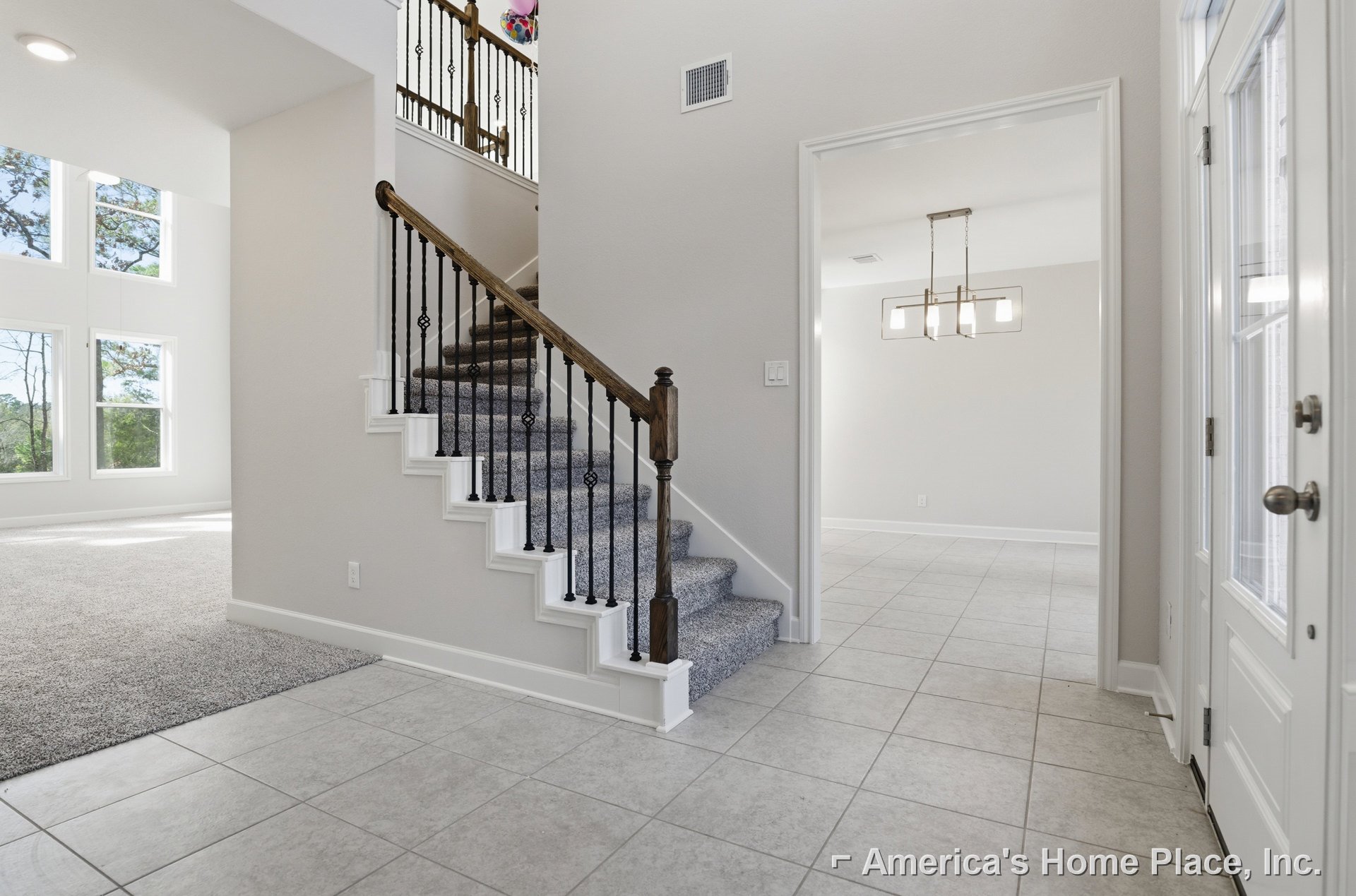 Carpeted staircase with black metal railing, white walls, door with silver knob, window showing leafy trees, and white vent on wall