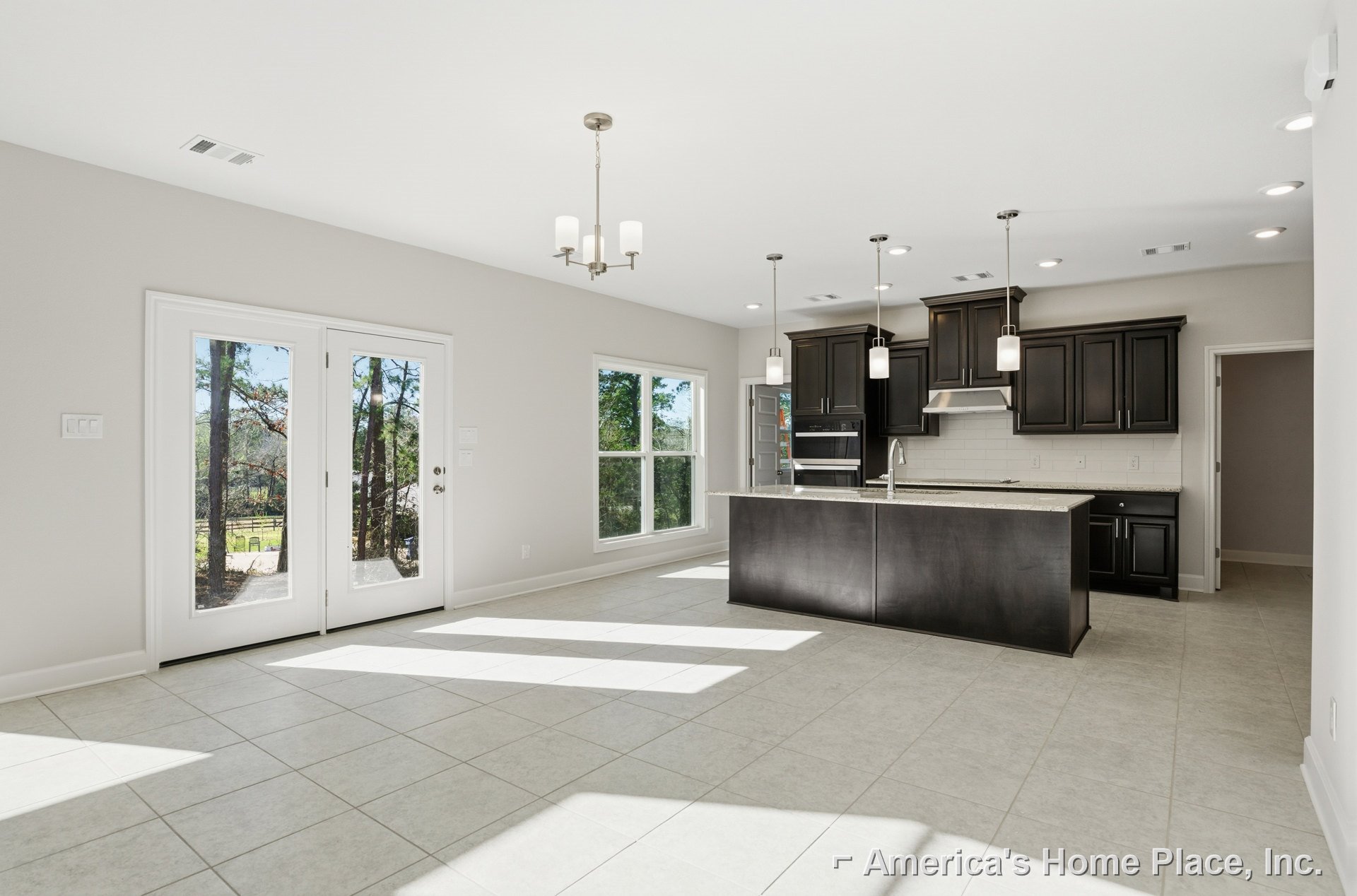 Bright kitchen featuring a central island with black countertop, white tile flooring, large window overlooking trees, modern cabinetry, and built-in sink.