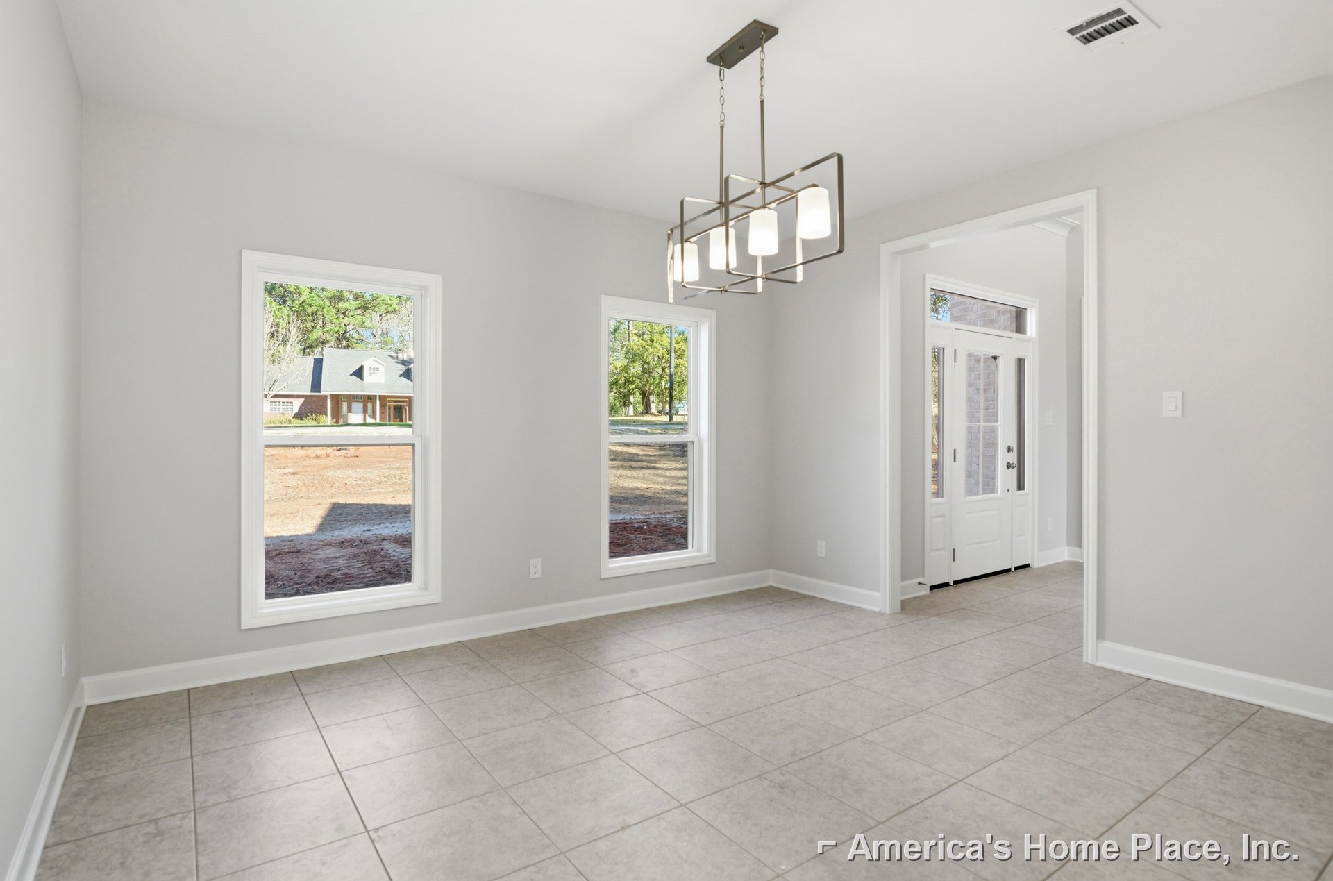 Chandelier with four lights hanging above white tile floor, large windows with view of neighboring house, white door with glass panel, plaster walls
