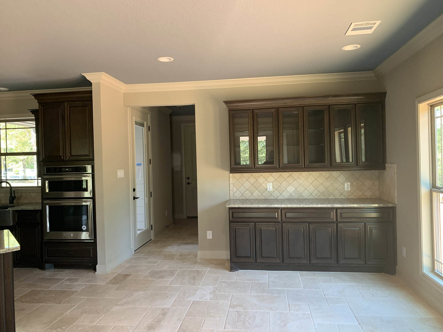 Kitchen with dark wood cabinets, stainless steel oven, tile flooring, white walls, vent, and a window above the countertop
