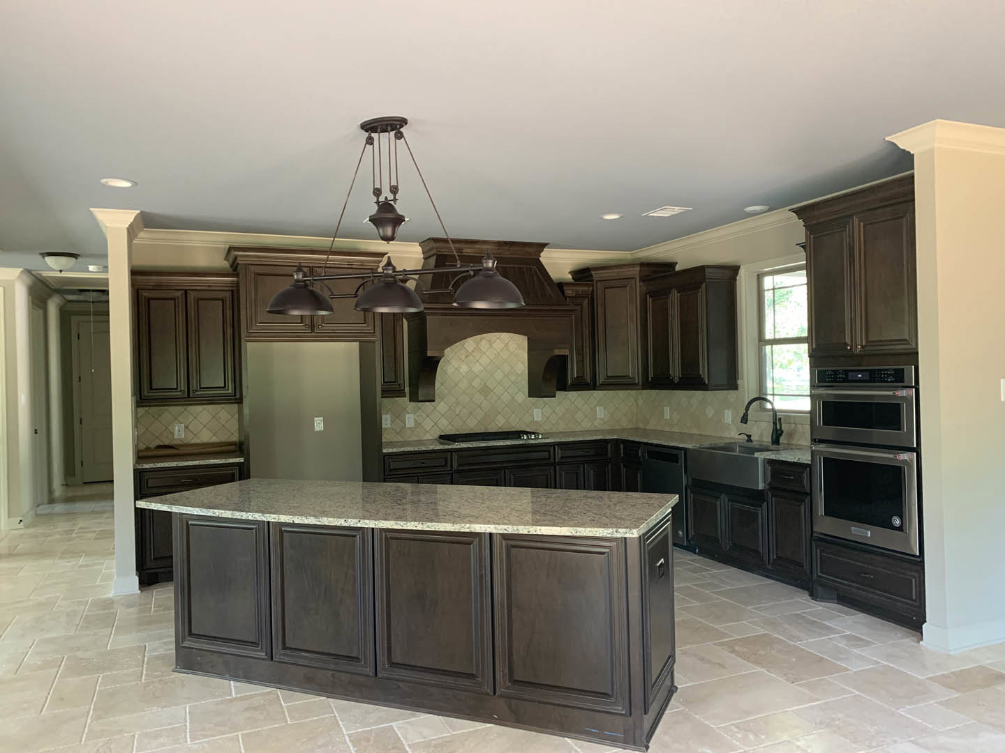 Spacious kitchen featuring a marble-topped island, white cabinetry, double oven, black curved faucet, pendant chandelier, and hardwood flooring