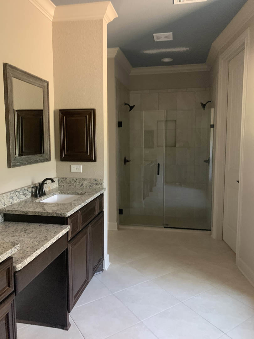 Bathroom featuring a glass shower door, wooden-framed mirror, brown door, white tile flooring, and chrome faucet