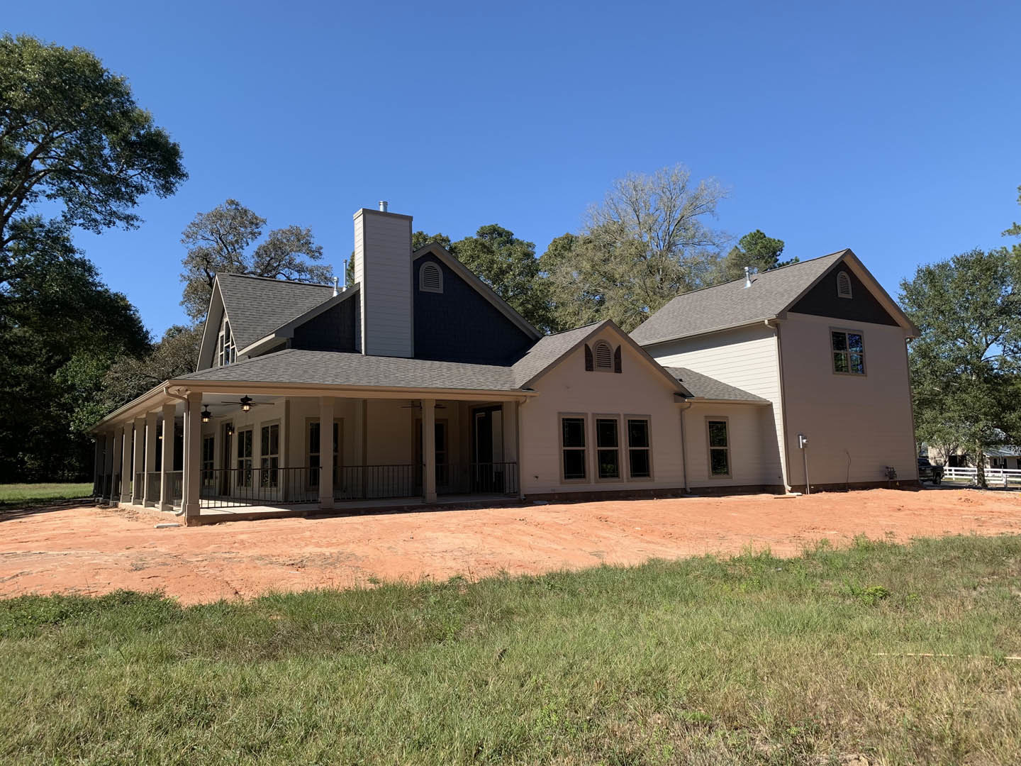 Wide front porch with white railings, multiple windows with white frames, brick chimney, manicured grass lawn, mature tree, evening sky