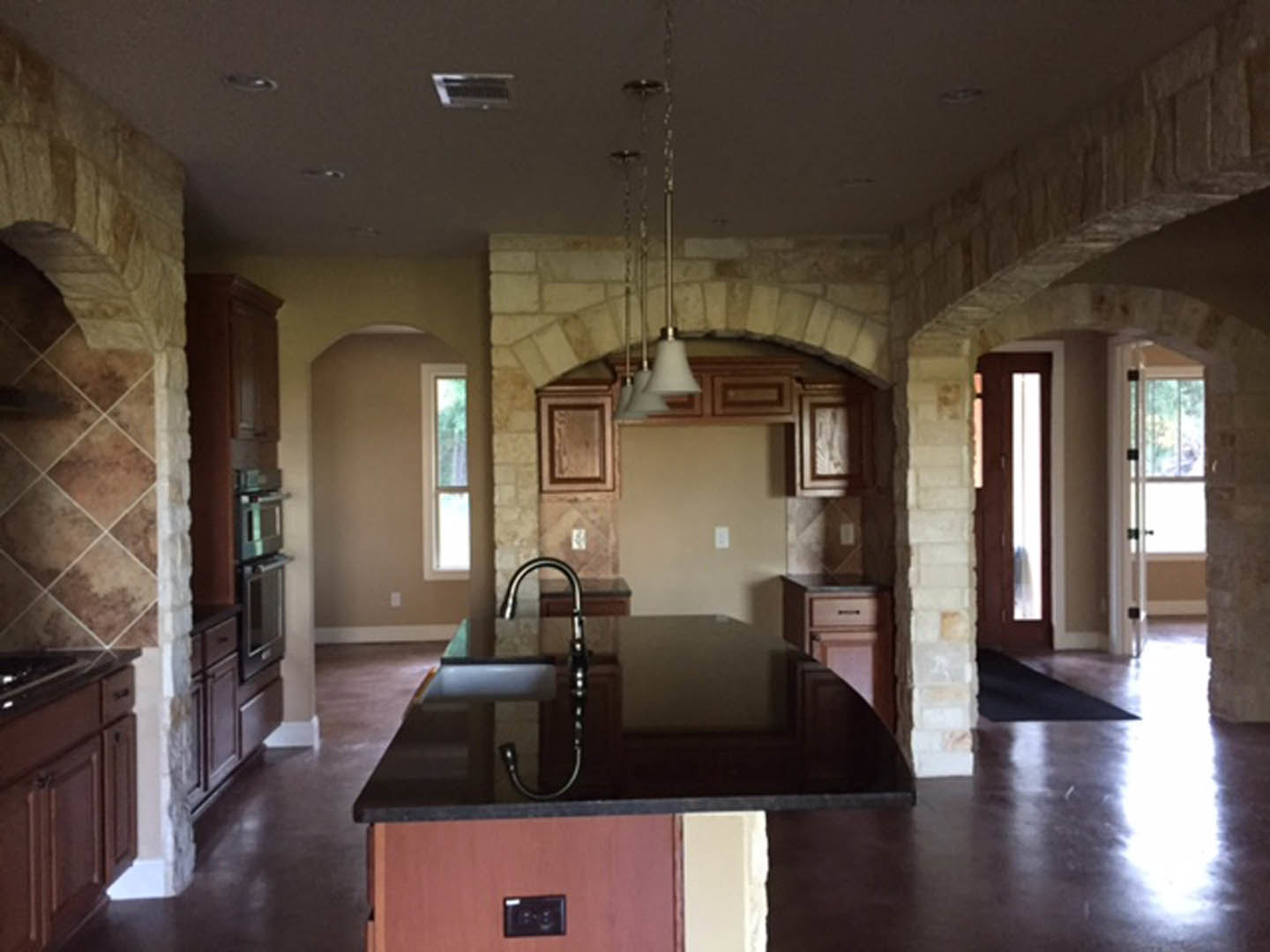Kitchen with textured stone walls, black countertop, modern cabinetry, lamp on counter, black outlet with two buttons, partial view of door, chain detail, and blurred train track