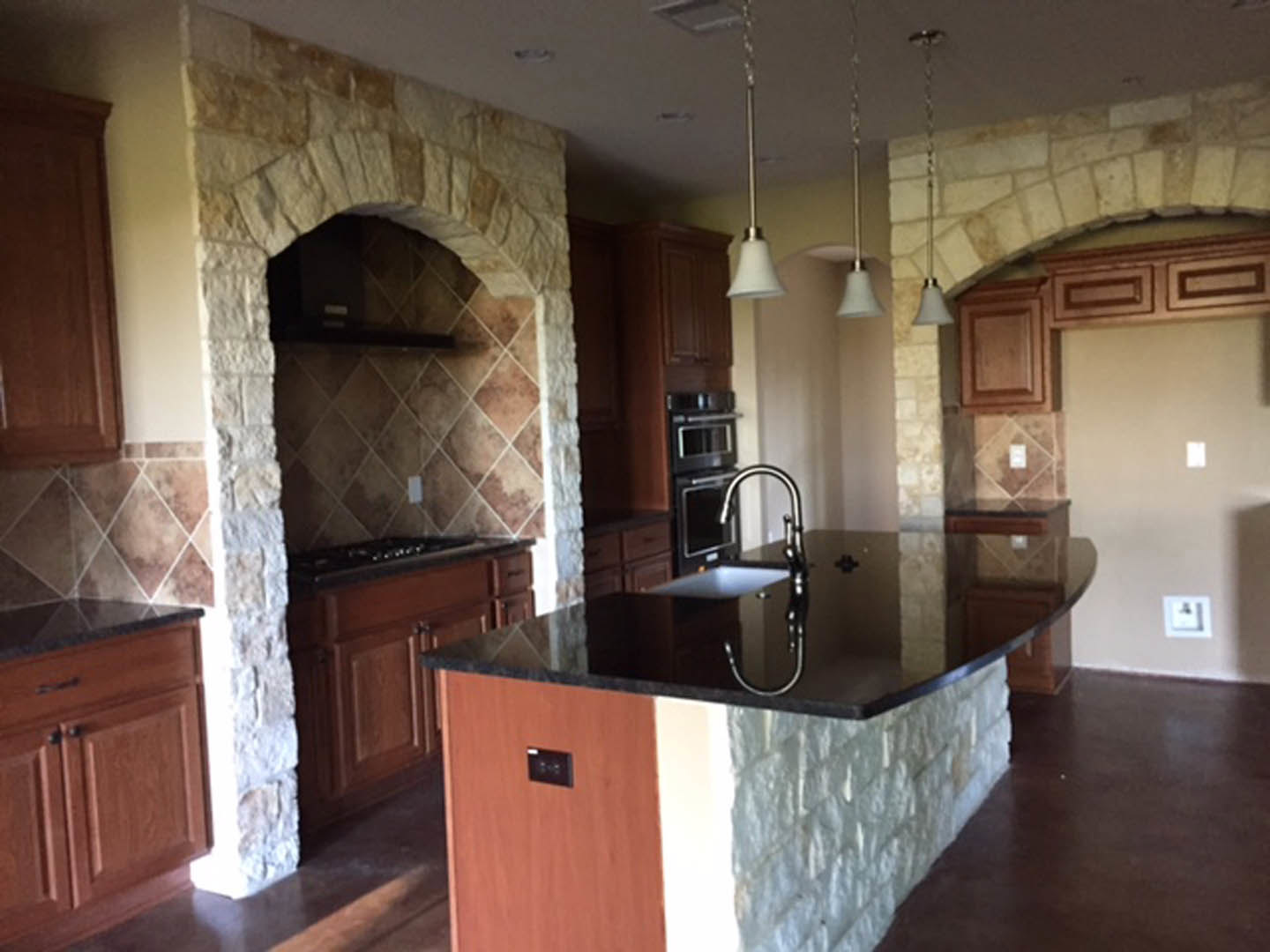 Kitchen with textured stone walls, black countertop, dark cabinetry, stainless steel sink, and modern lighting fixtures