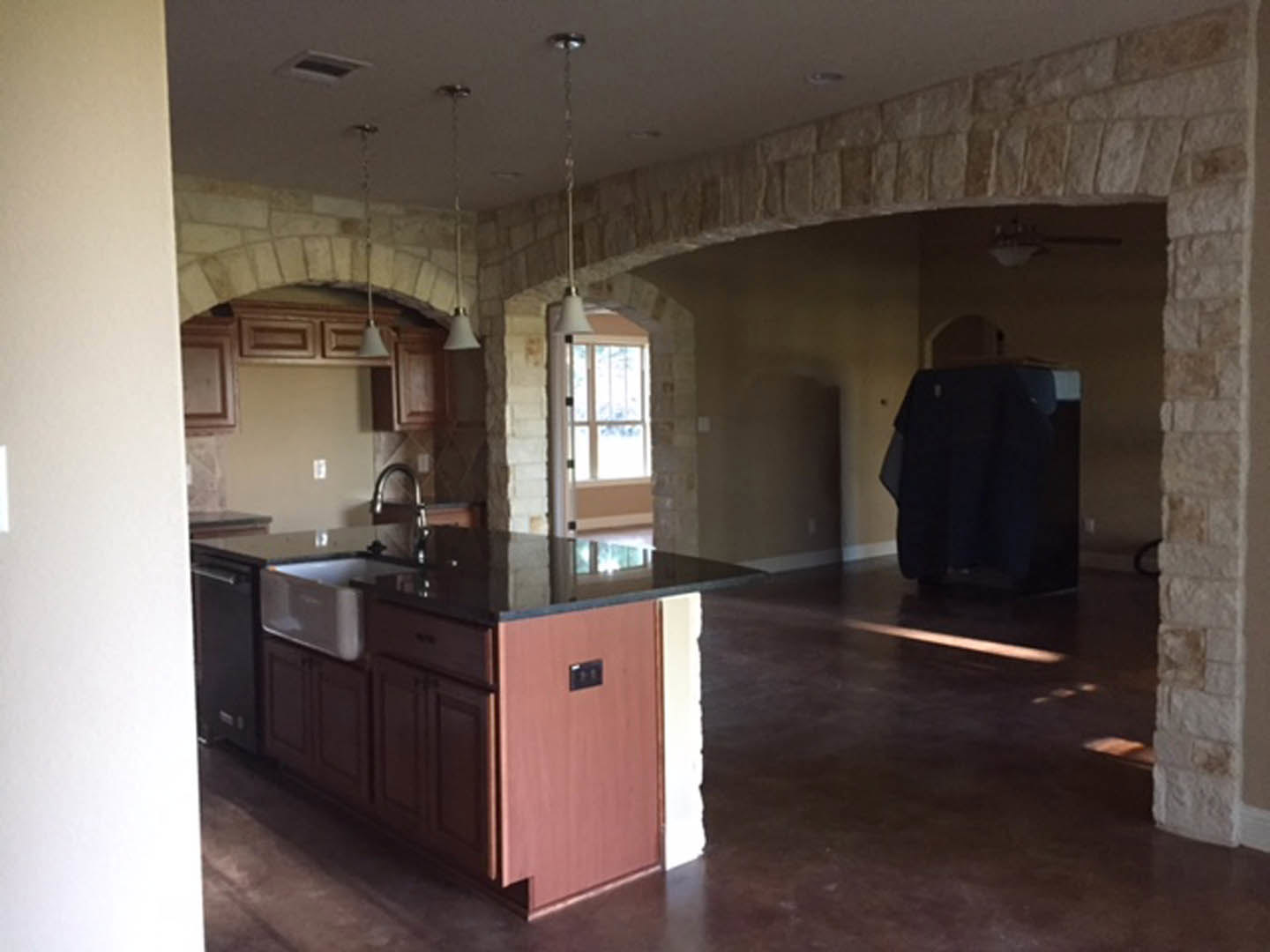 Kitchen featuring textured stone walls and a prominent stone archway, white cabinetry, stainless steel sink, dark-edged countertop, and recessed ceiling vent