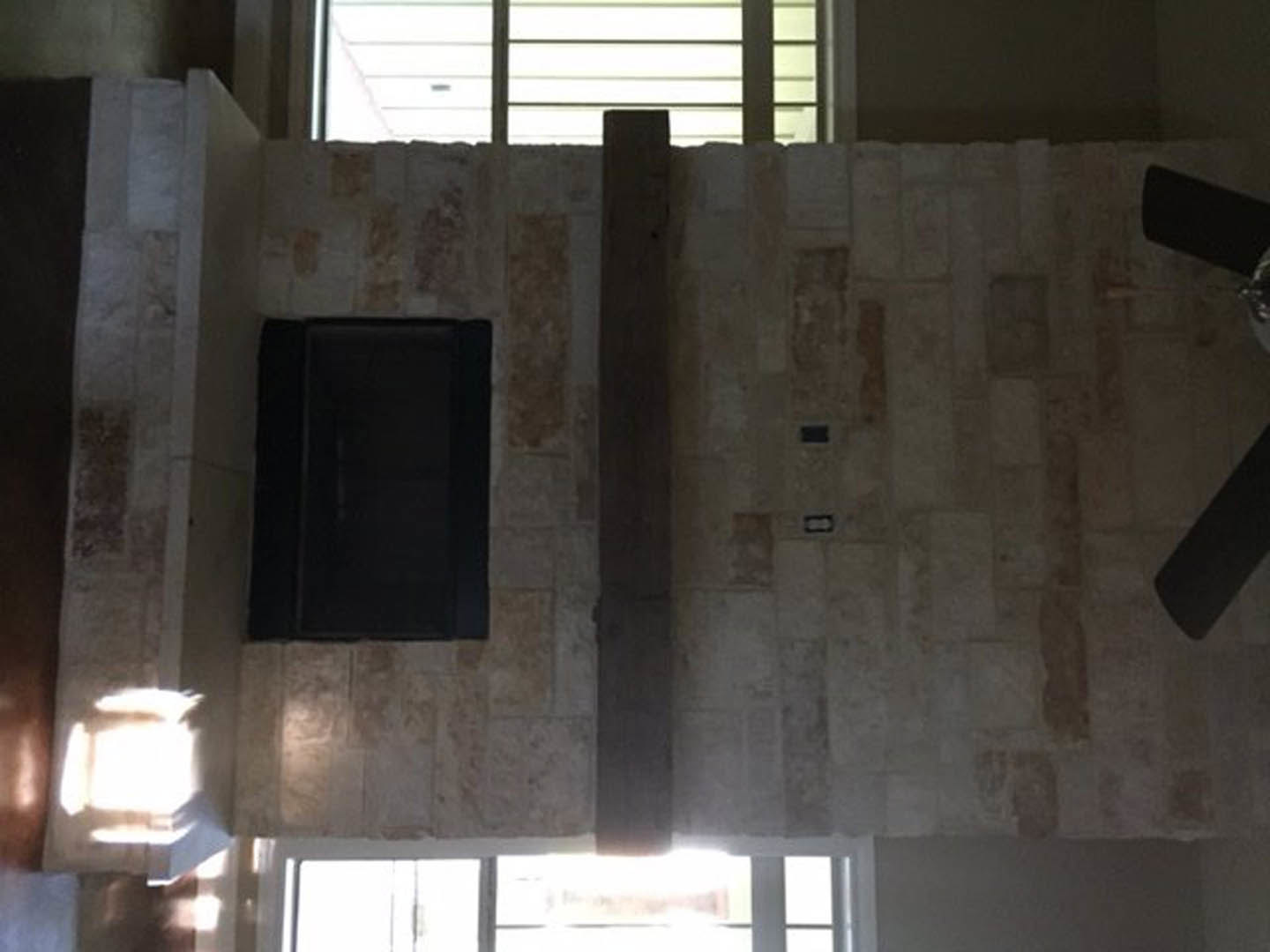Stone fireplace with white plaster surround, large window with daylight, light-colored walls and ceiling, person standing near window