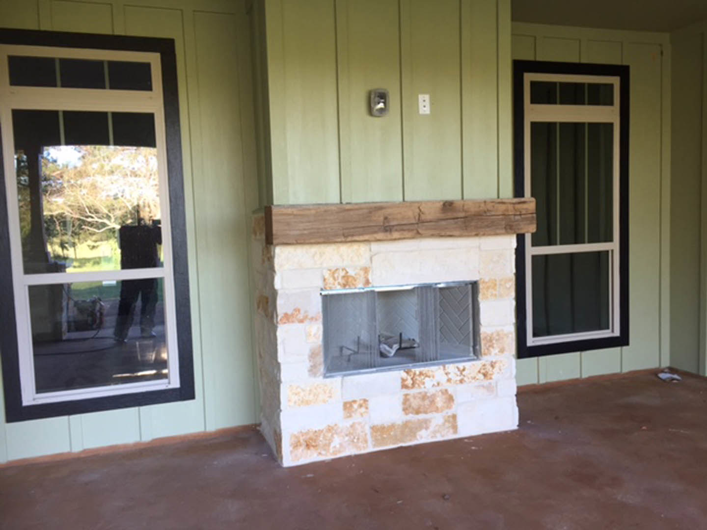 Stone fireplace with glass door, white-framed screen door, large window reflecting a person, wood floor, and light switch on wall
