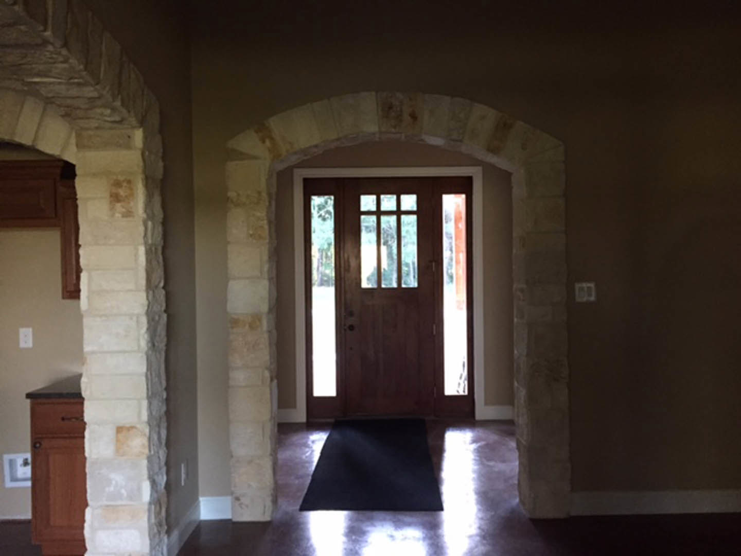 Wooden door with glass panes set in a stone archway, adjacent to a window, opening onto hardwood flooring in a residential interior.