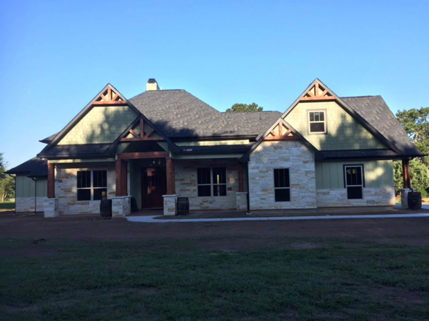 Two-story house with white-framed windows, covered front porch, wooden door, and green lawn bordered by trees under a blue sky