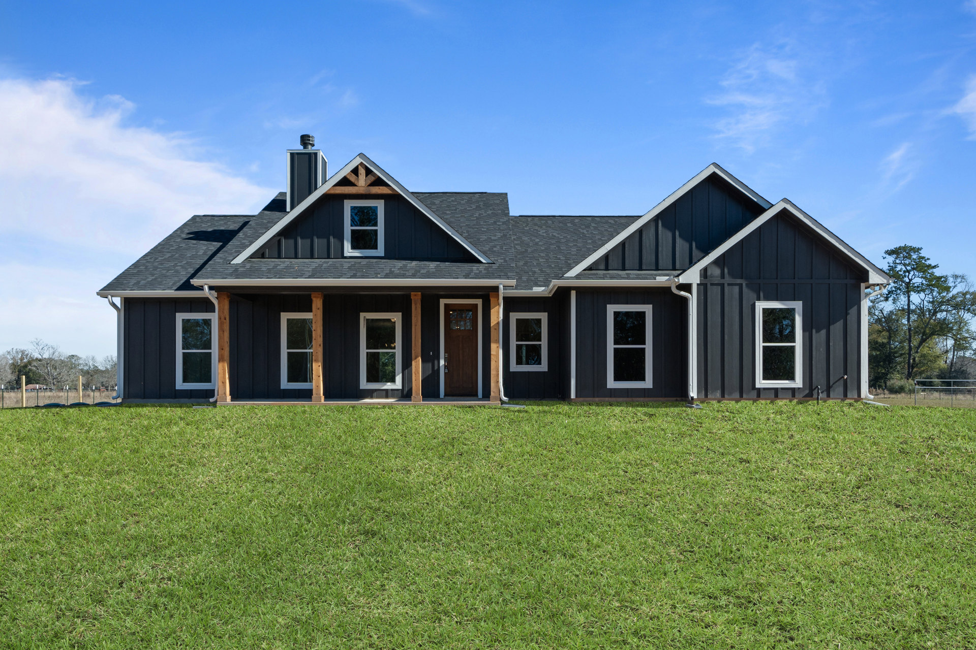 White-trimmed windows and front door on a modern house, surrounded by green grass lawn, porch, and mature trees under a partly cloudy sky