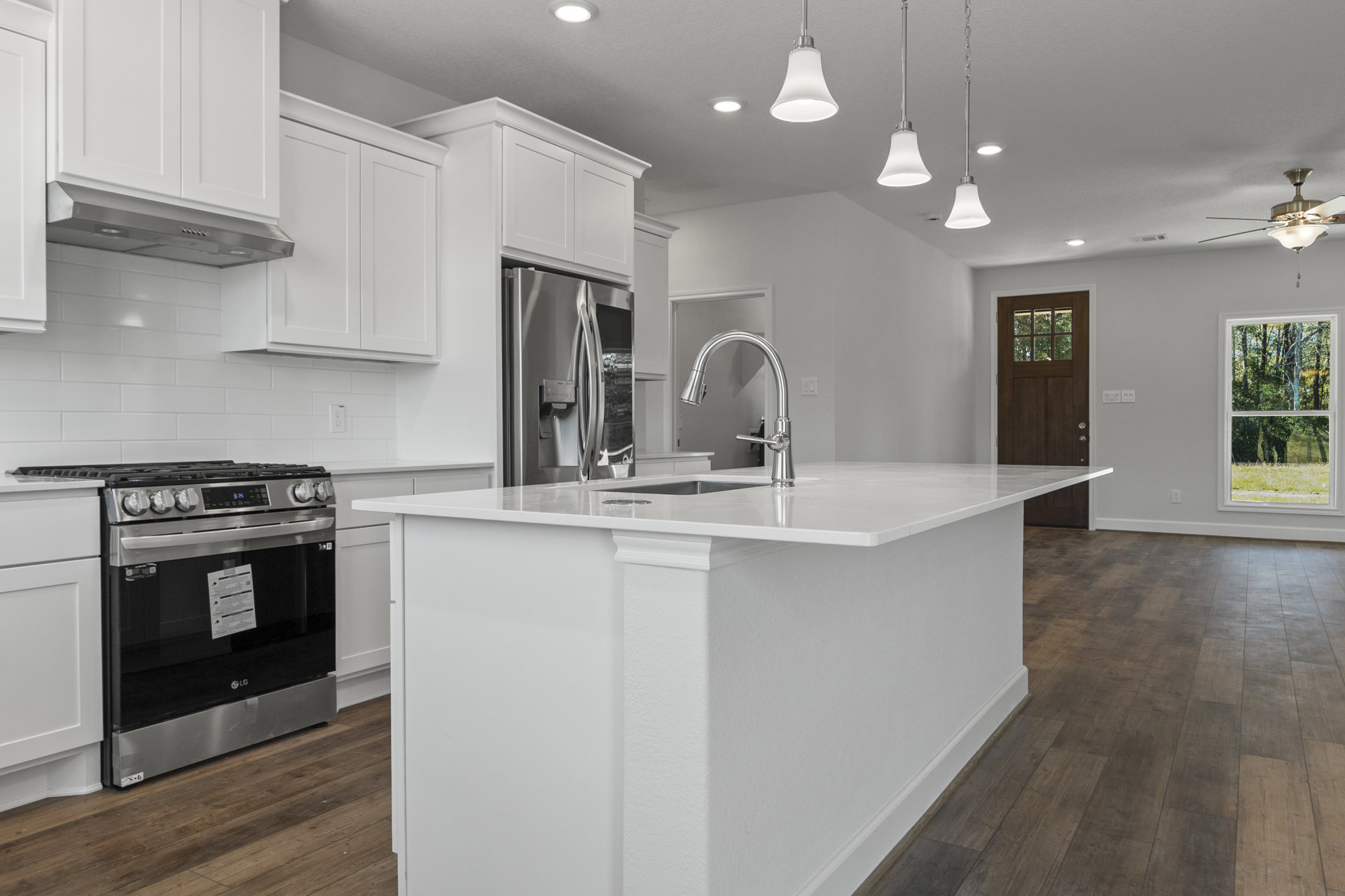 White kitchen island with chrome faucet, stainless steel stove and refrigerator, white cabinetry, large window overlooking trees, light countertops and flooring