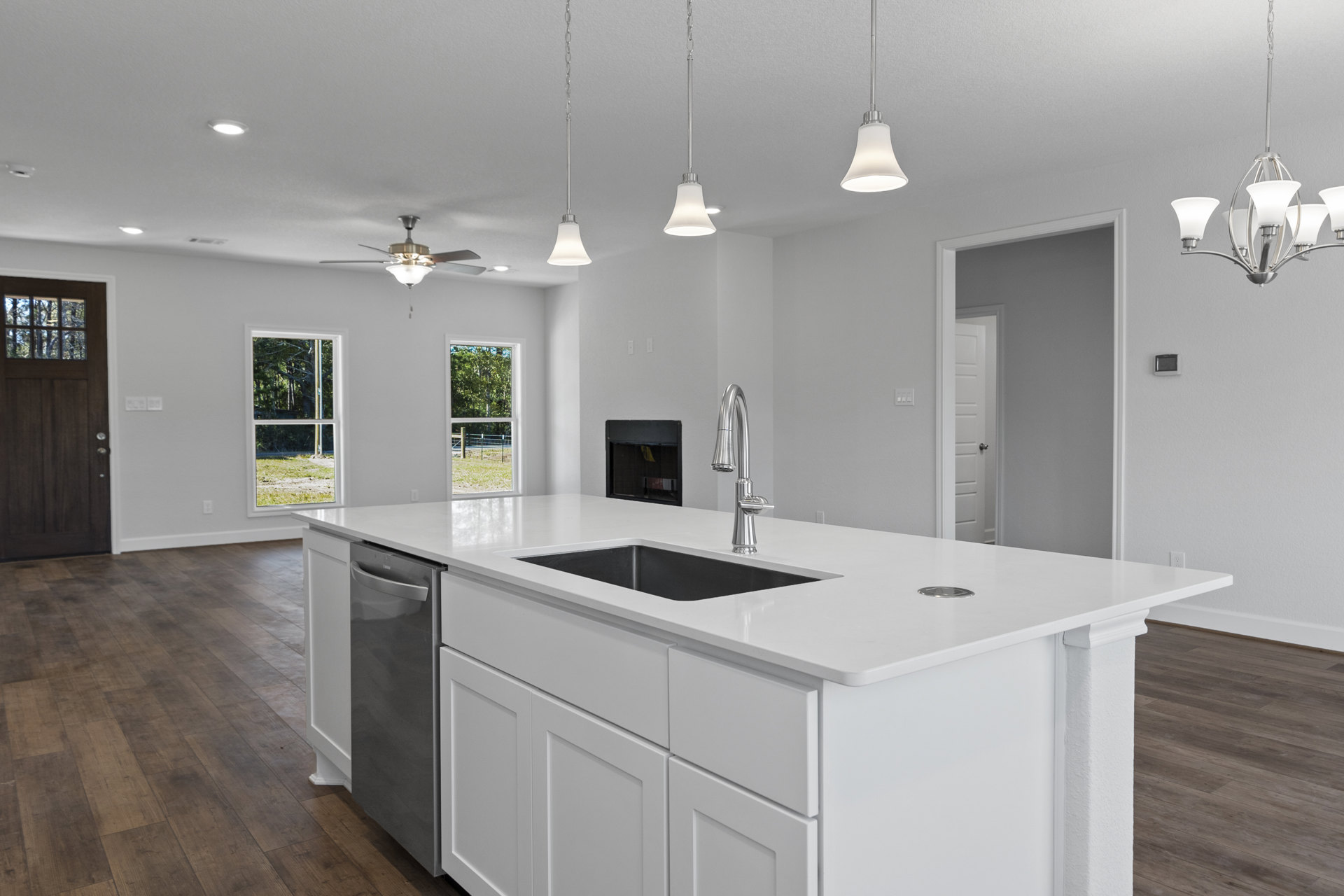 White kitchen with a central island featuring a built-in sink, stainless steel stove, white cabinetry, light countertops, and modern pendant light fixtures