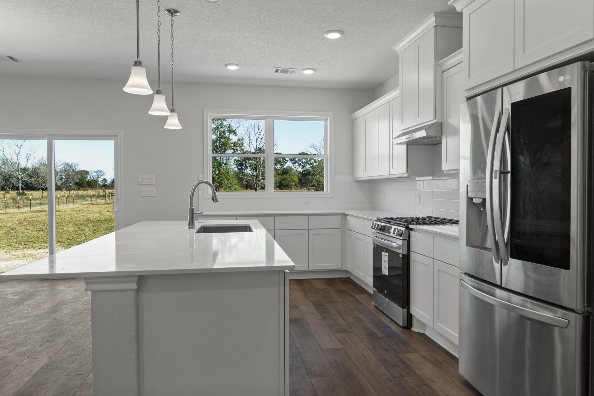 White kitchen with shaker cabinets, stainless steel refrigerator, black and silver oven, white island with stainless steel faucet, tile backsplash, window overlooking trees, and
