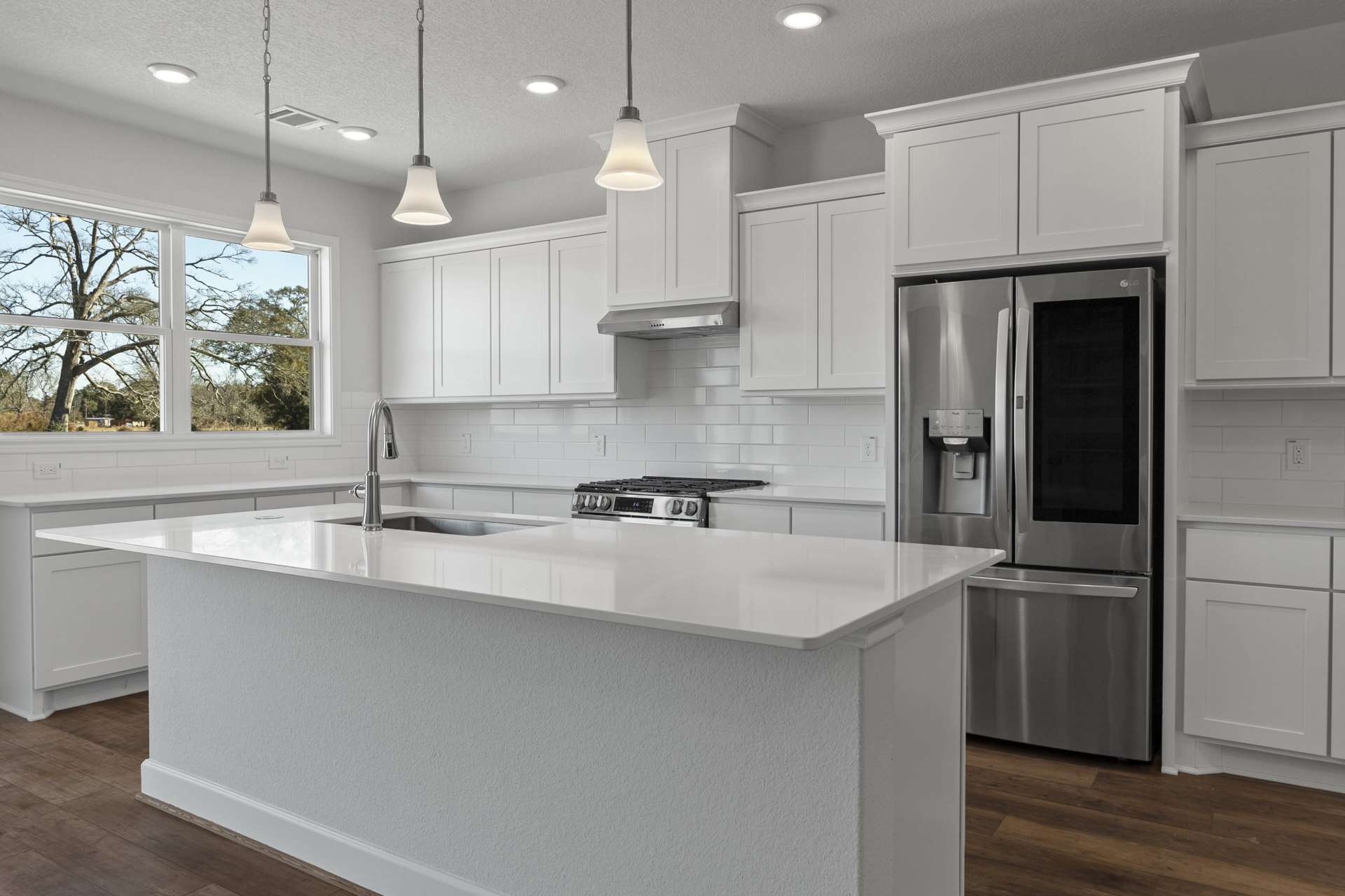 White kitchen cabinets, granite countertops, stainless steel refrigerator with ice and water dispenser, tile backsplash, built-in sink, and stove.