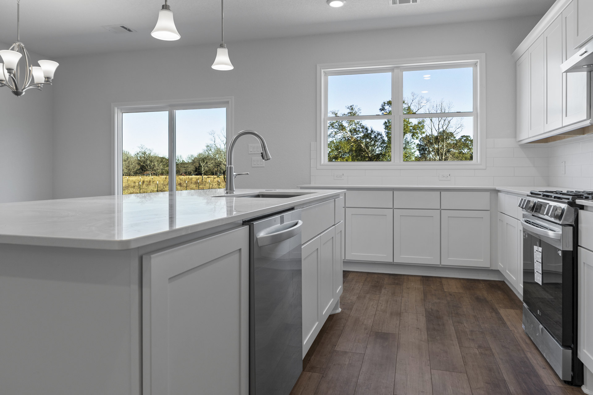 White kitchen cabinets, stainless steel sink with silver faucet, black and silver refrigerator with white sign, wood flooring with white trim, window overlooking trees, close-up of