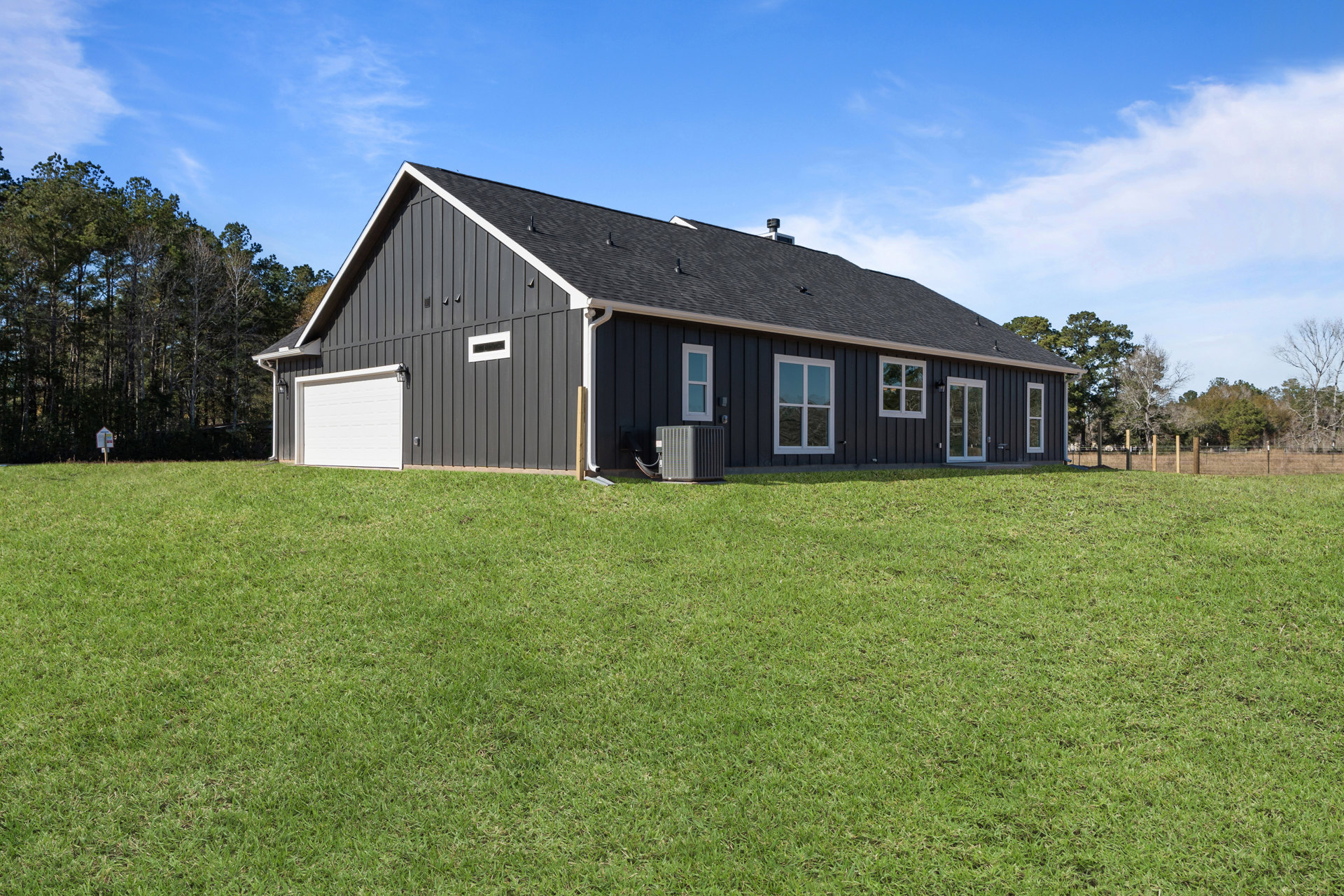 Two-story farmhouse with white siding, black accent wall, white garage door, large windows with white frames, gray air conditioning unit and heater on exterior, expansive green