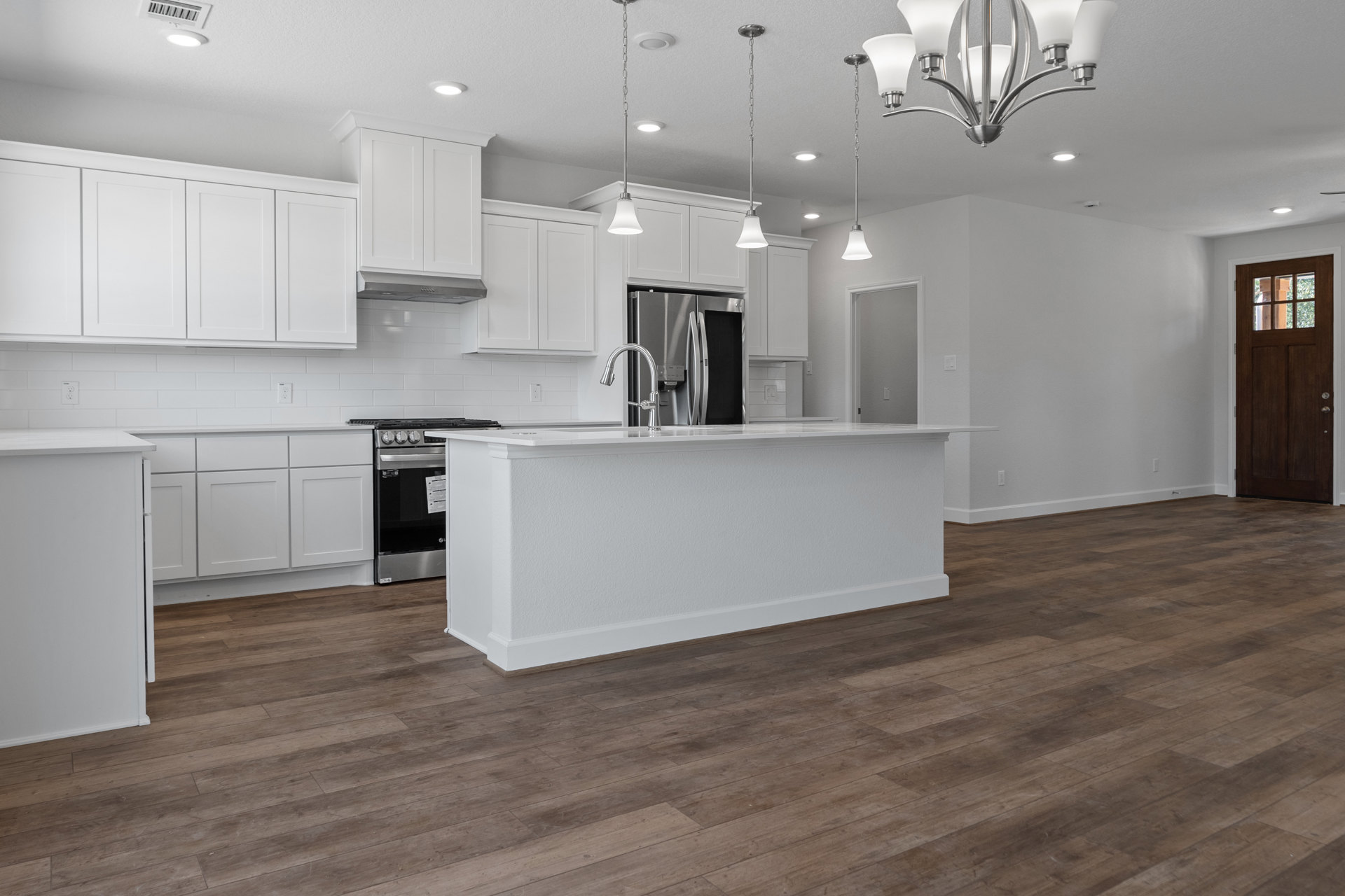 Kitchen with wide-plank wood flooring, white shaker cabinets, white quartz countertop, stainless steel refrigerator, modern chandelier, and white walls