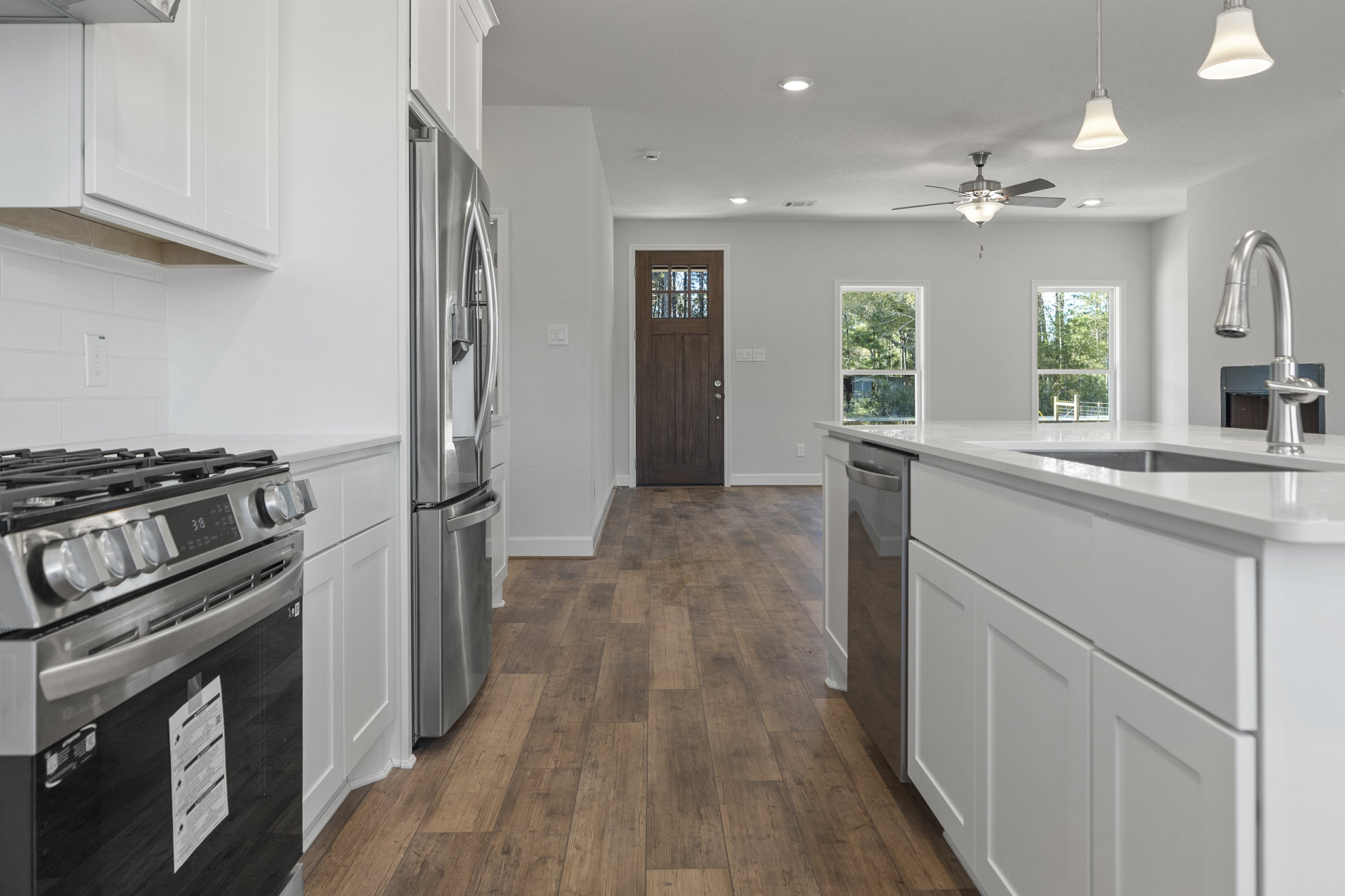 White kitchen with shaker cabinets, wood plank flooring, stainless steel stove and refrigerator, pendant light fixture, and a central island featuring an undermount sink