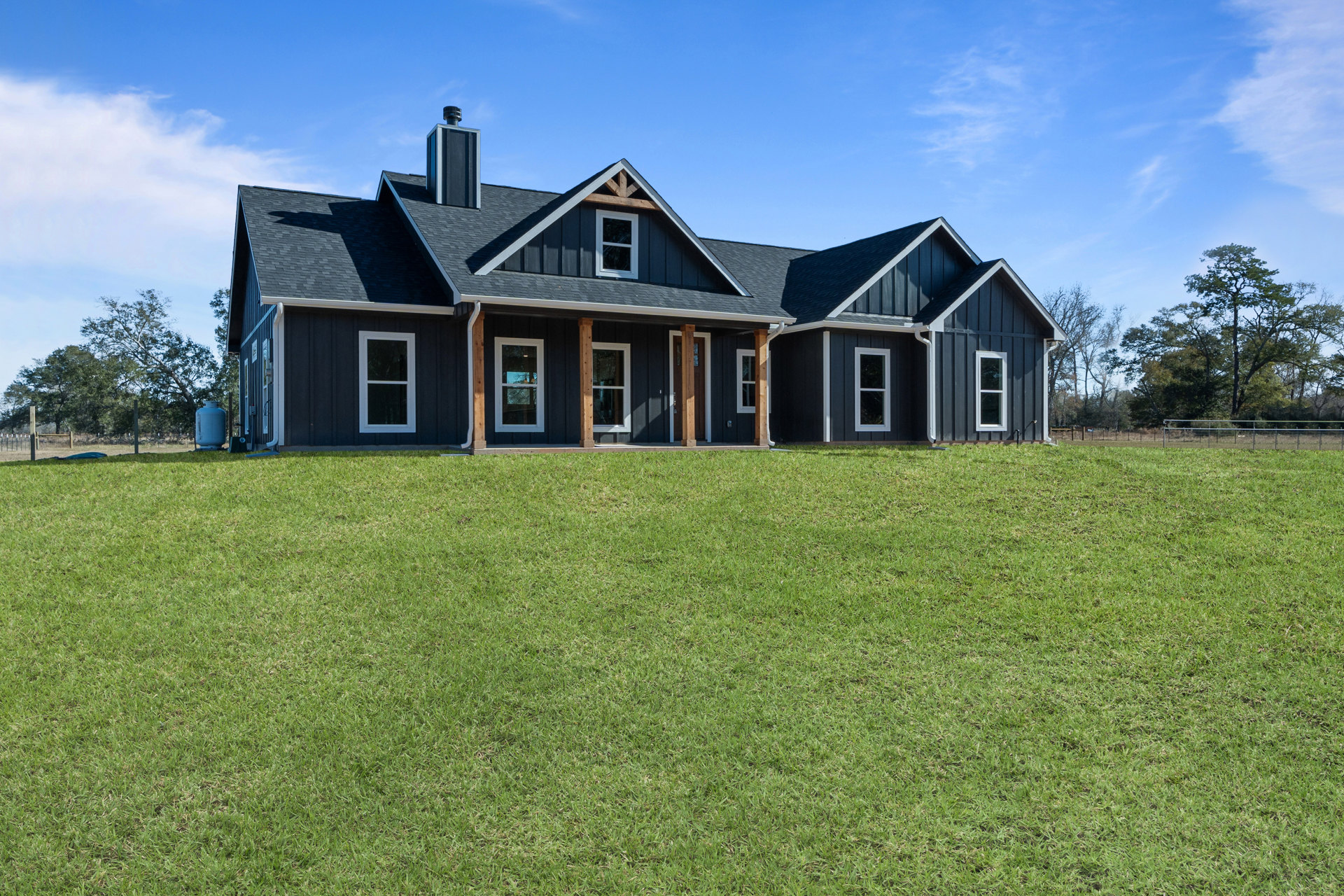 Two-story home with white-framed windows, covered porch, gray roof, and manicured green lawn under a blue sky with scattered clouds