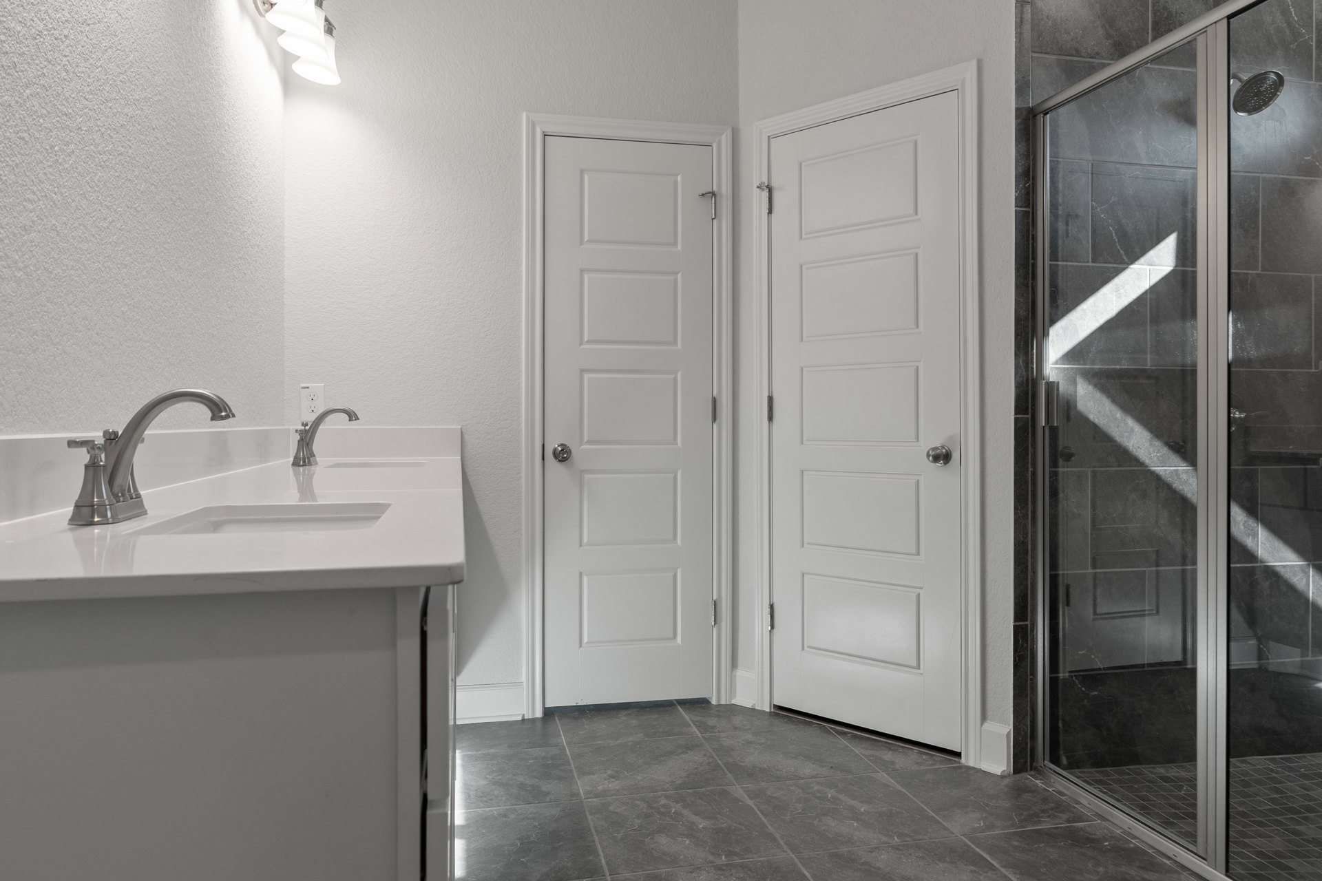 Bathroom with white paneled doors, silver doorknobs, glass shower door, tiled walls, modern sink and faucet, wall-mounted mirror, and overhead lighting.