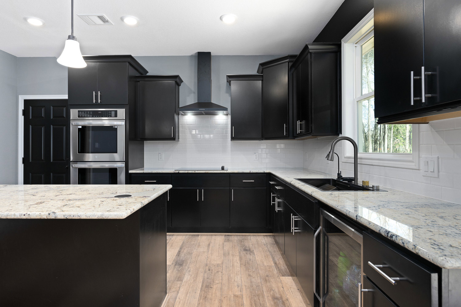 Modern kitchen featuring black cabinetry with silver handles, white countertops, stainless steel oven, black door, and contemporary lighting fixtures
