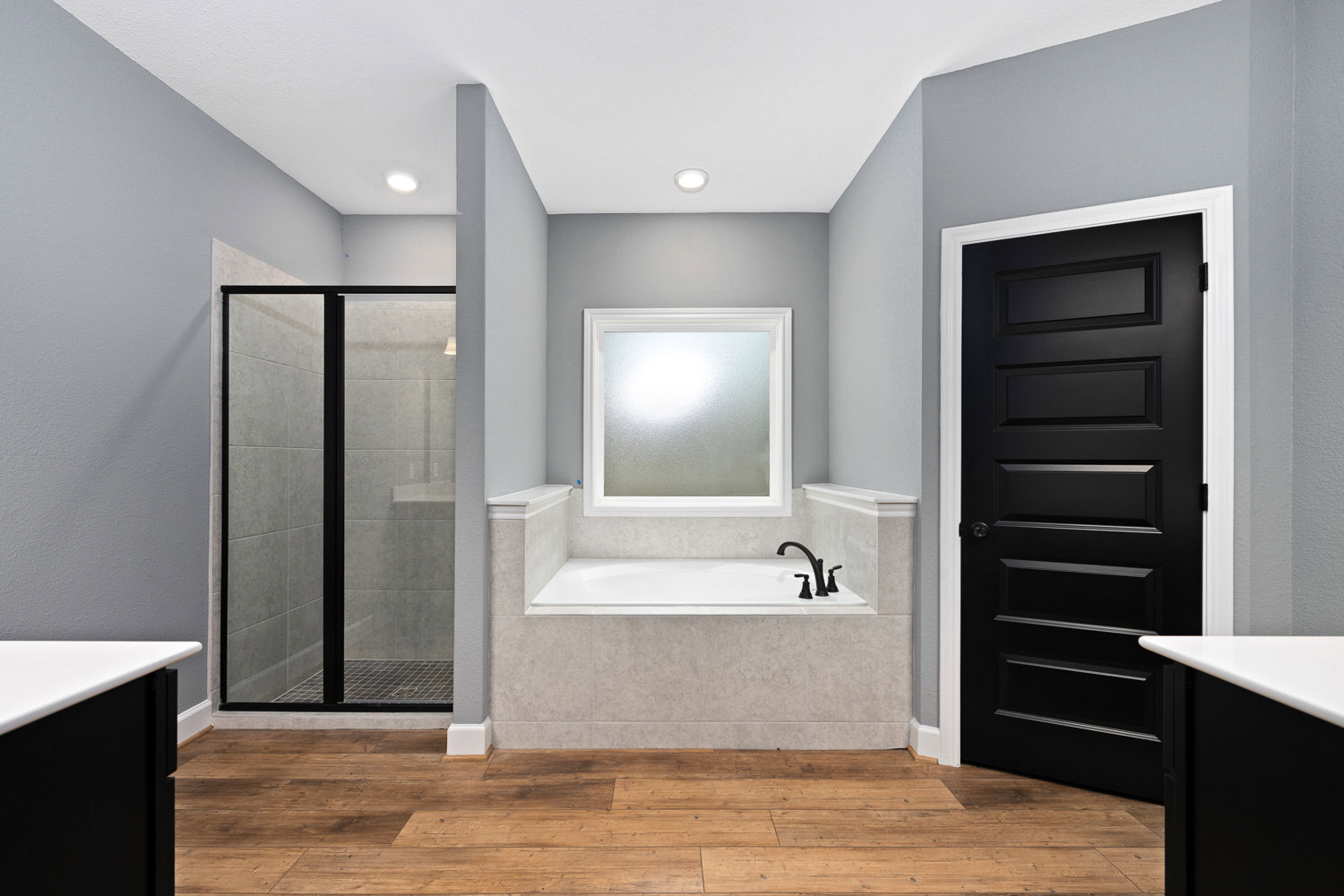 Bathroom featuring a freestanding bathtub and glass-enclosed shower, wood flooring, white tile walls, black door with white trim, frosted glass window, and black and white