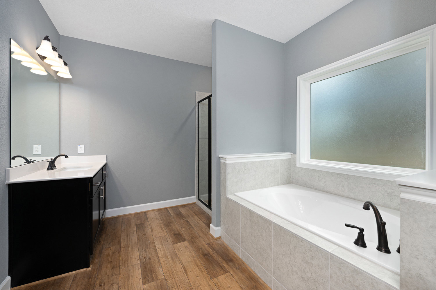 Modern bathroom featuring a freestanding white bathtub, rectangular sink with chrome tap, black and white tile flooring, frosted glass window, and wall-mounted row of lights.