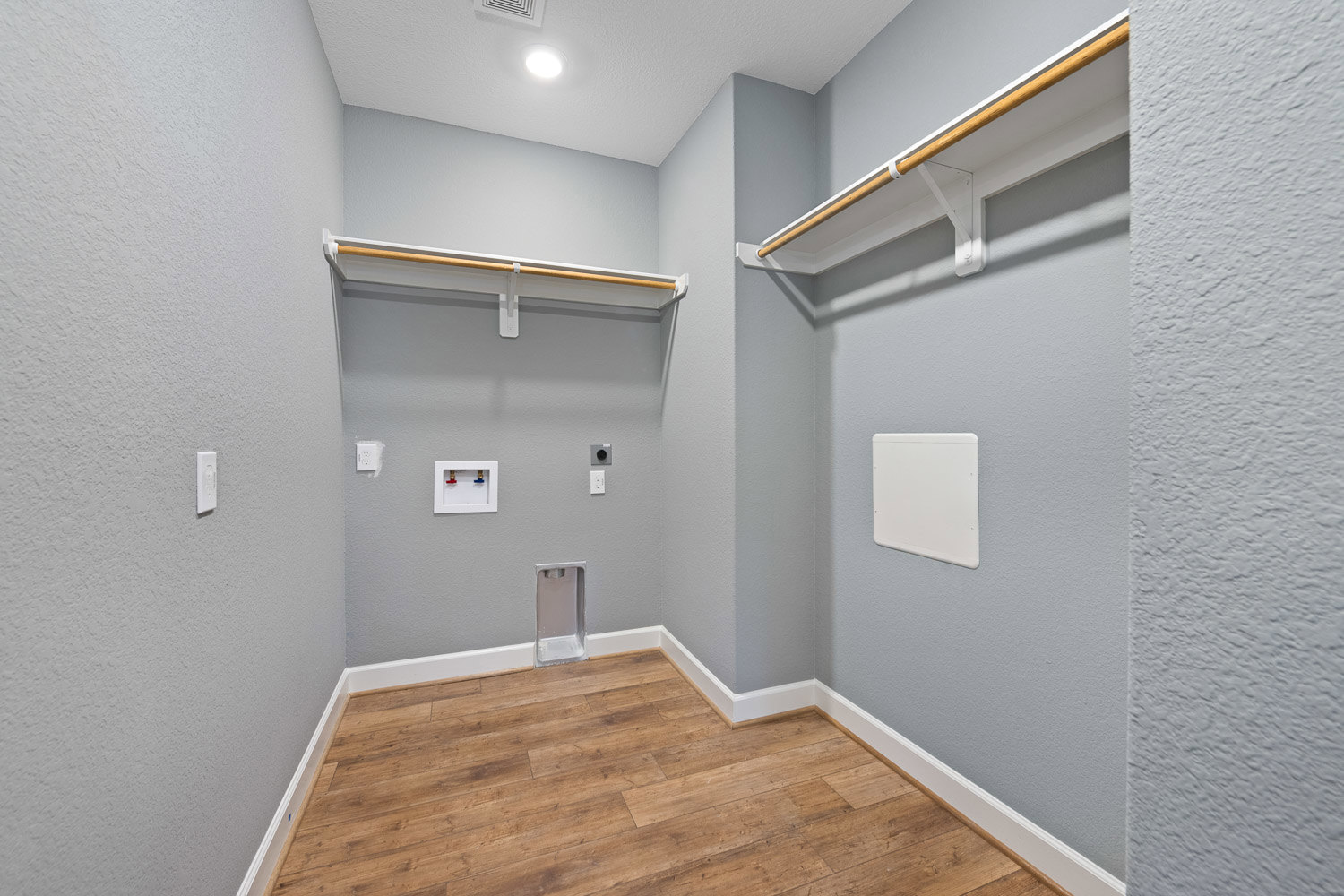 Wood plank flooring with white baseboards, built-in white shelving unit on wall, white rectangular cabinet with black handle, white box featuring red and blue handles, recessed