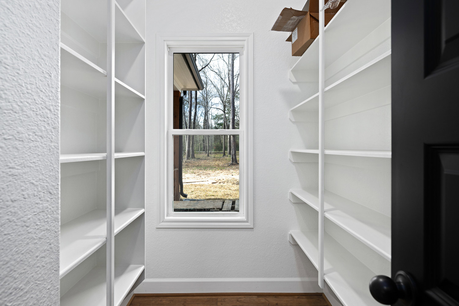 Built-in white shelving along plaster walls, wood surface detail, window overlooking leafy trees, brass door knob in foreground