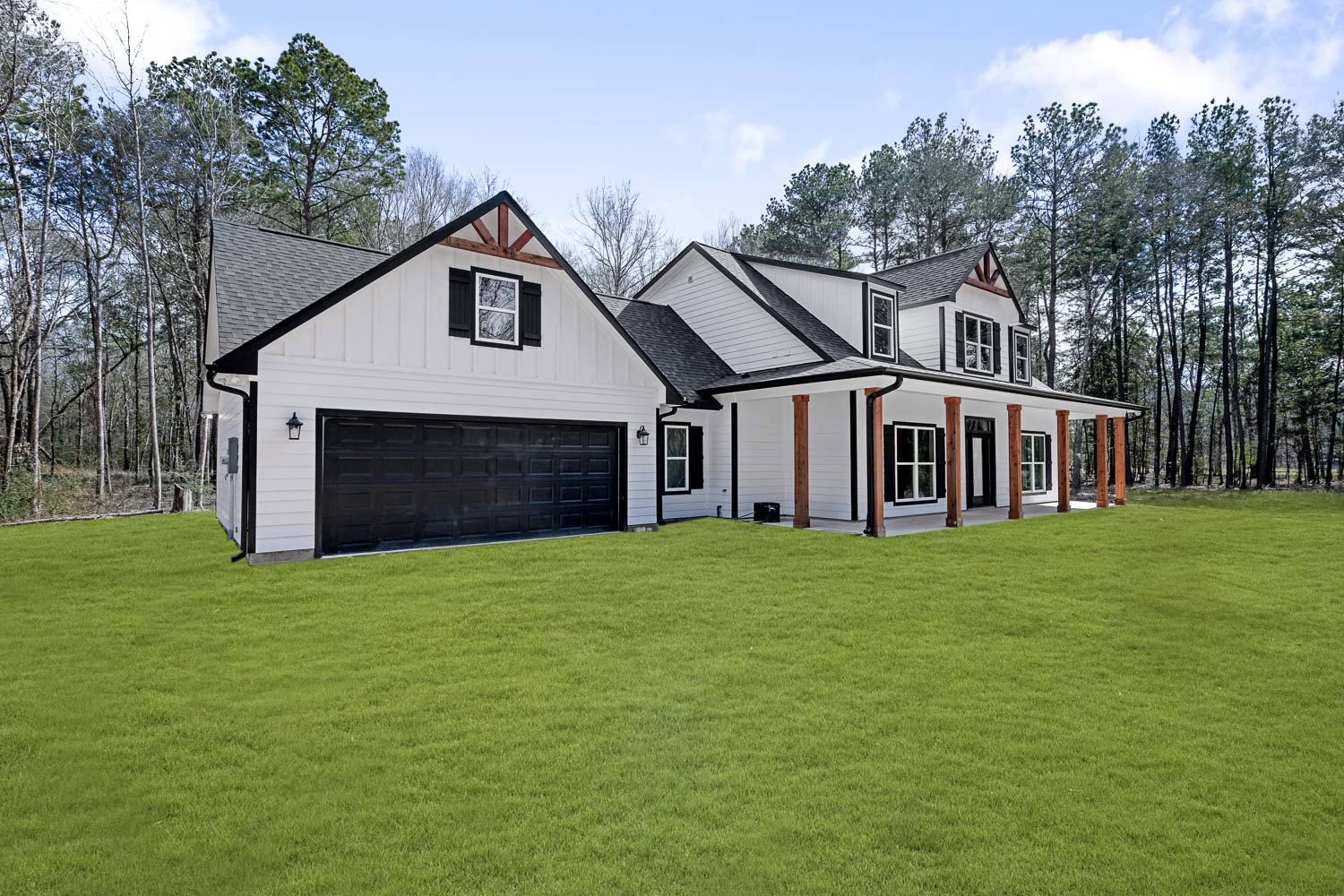 Modern house with black garage door, white roof, large window with white frame, manicured green lawn, and mature trees under partly cloudy sky