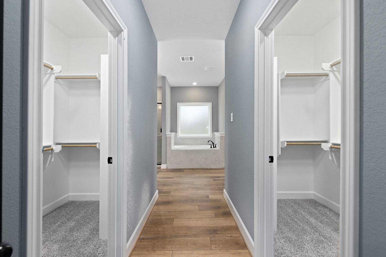 Hallway with wood flooring and white trim, white framed square window, built-in closets with shelves and doors, freestanding bathtub, white walls and ceiling