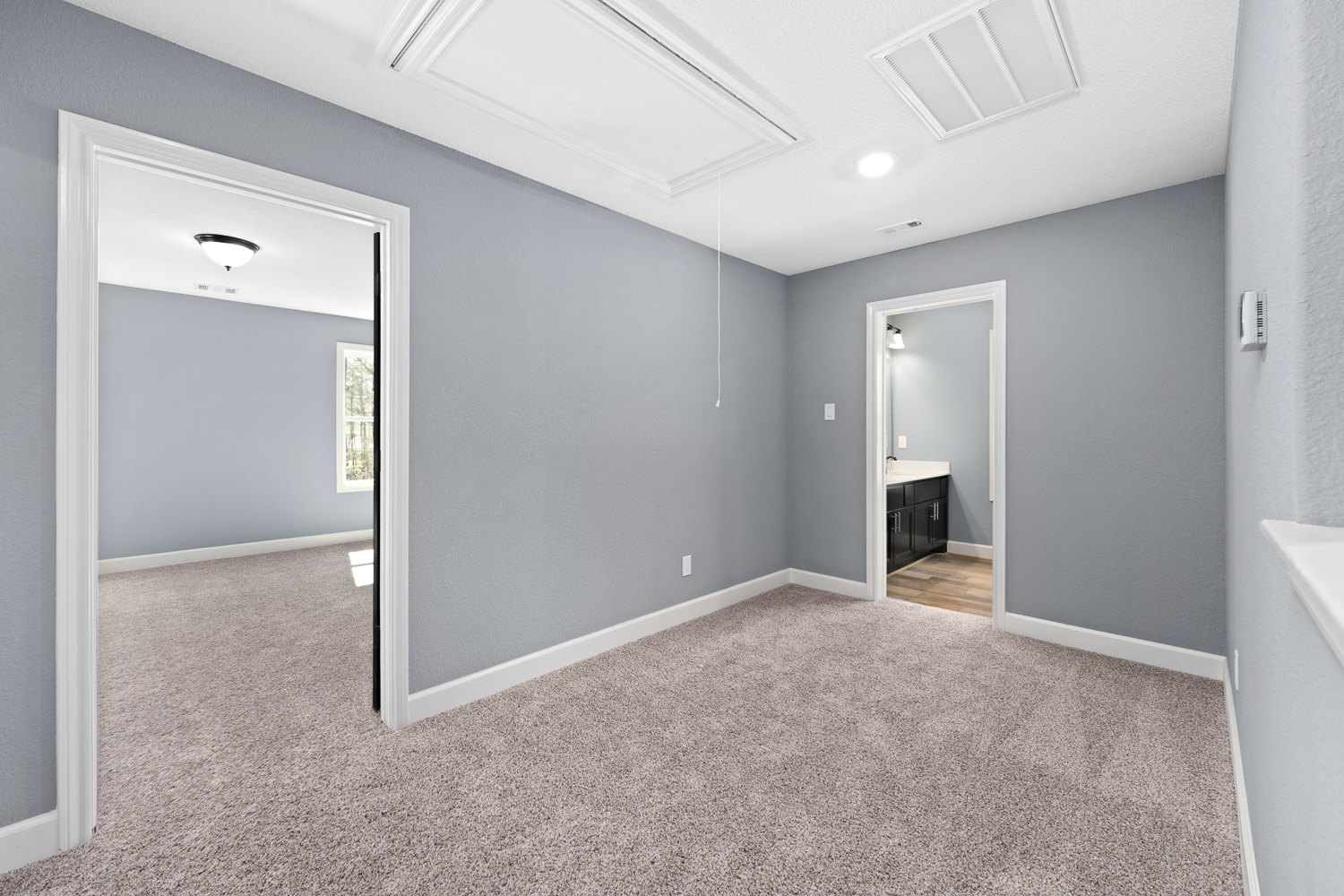 Bedroom with beige carpet, white grid ceiling with molding, open white door leading to bathroom, light-colored walls