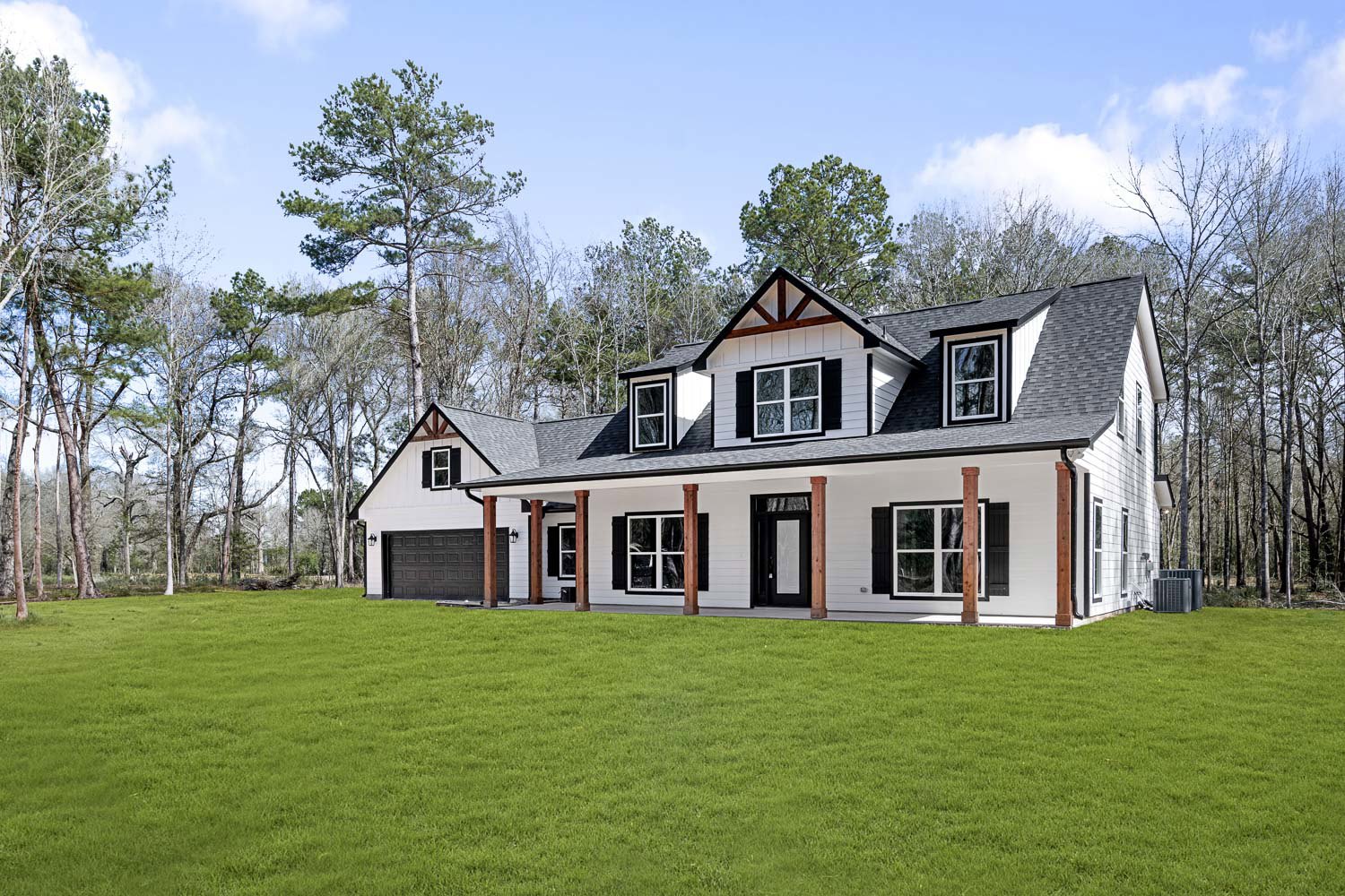 White two-story house with black shutters, front porch supported by white columns, manicured green lawn, tall leafy tree and smaller trees in foreground, multiple windows with