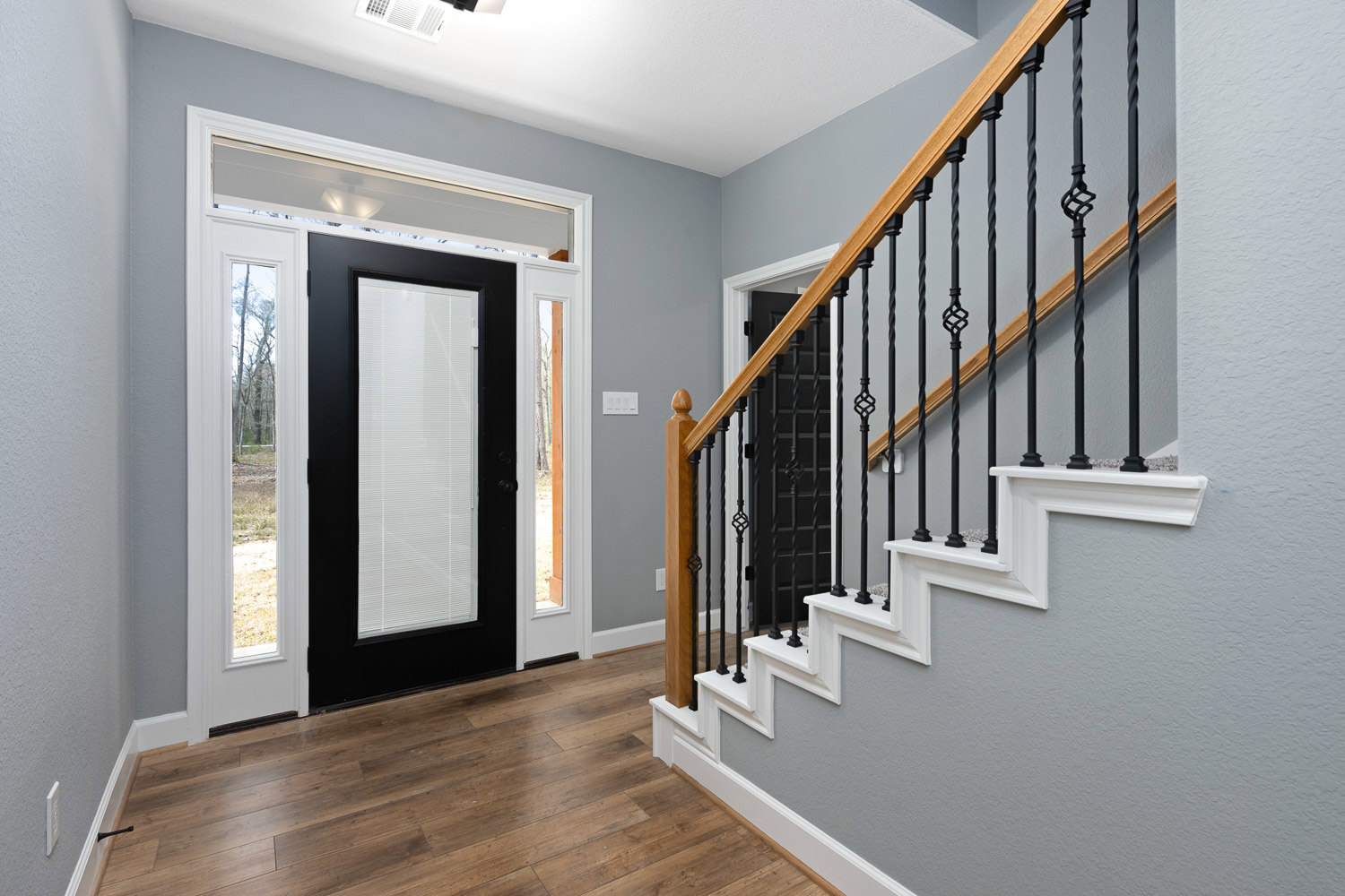 Wood staircase with black metal railings, black-framed glass door, white walls, and light wood flooring in a modern home entryway