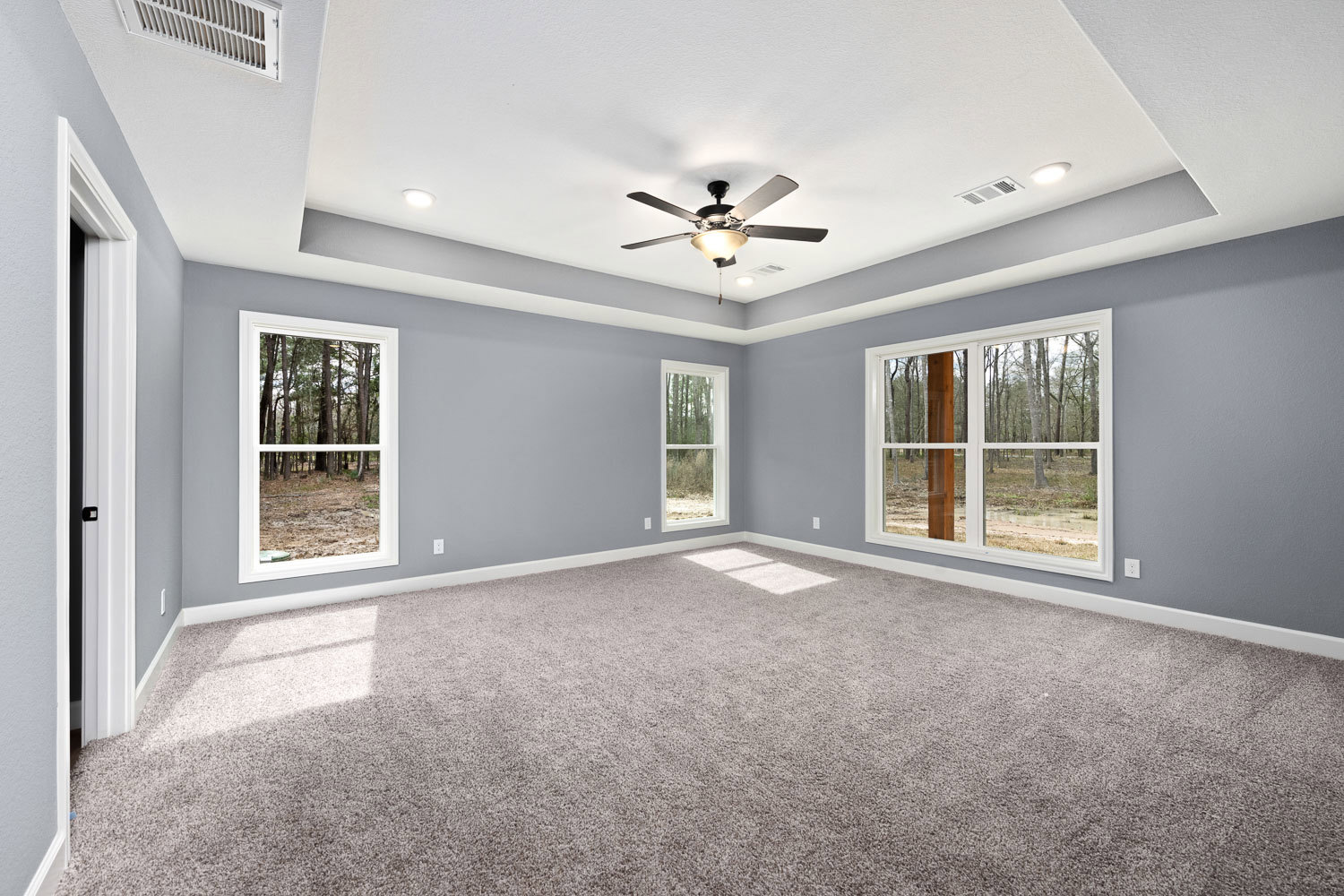 Carpeted room with white walls, ceiling fan with light fixture, large windows overlooking green trees and forest