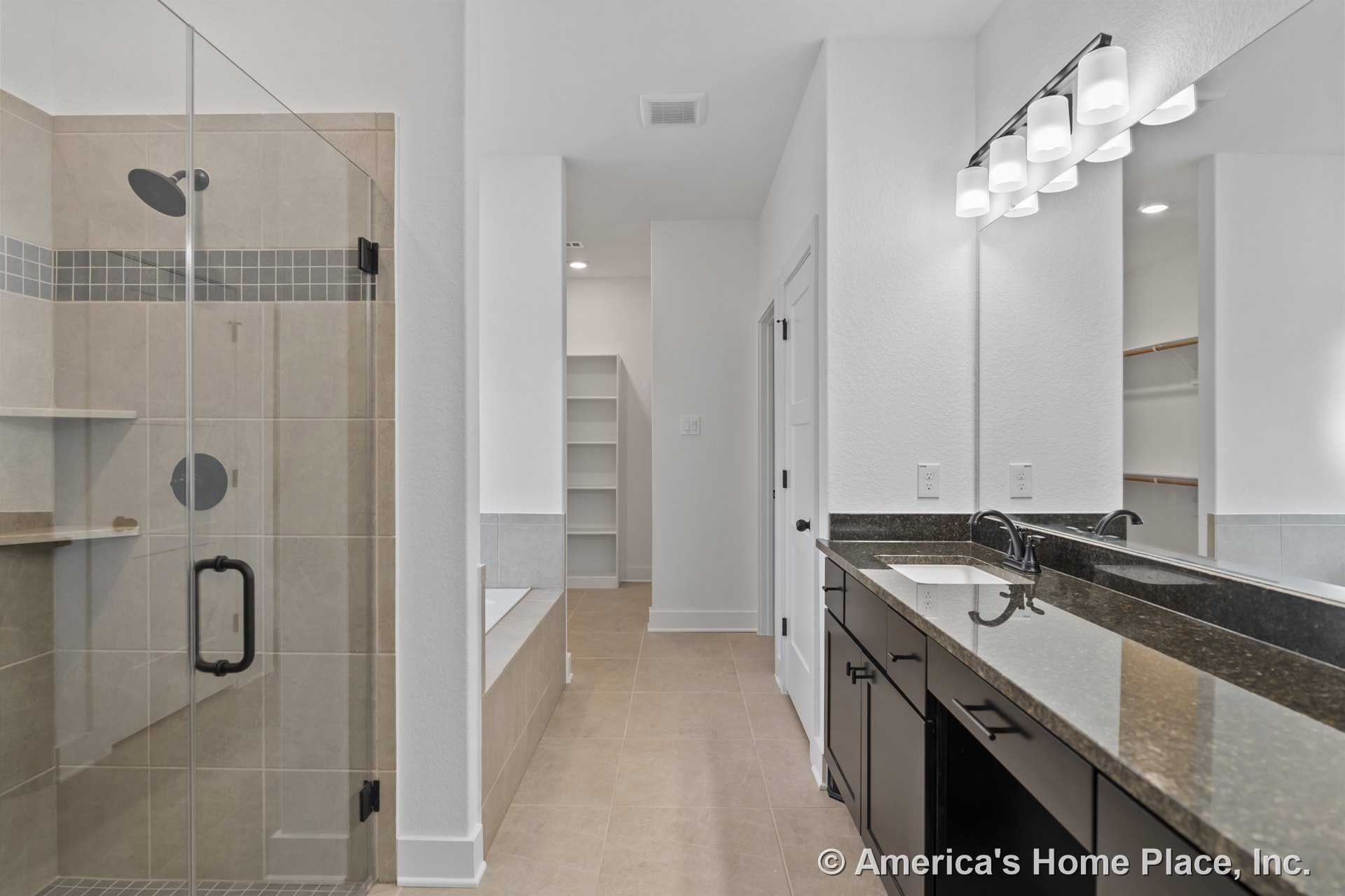 Glass-enclosed shower with tile flooring, double vanity featuring dark wood cabinetry and granite countertops, built-in shelving, modern vanity lighting, large mirrors, and dual
