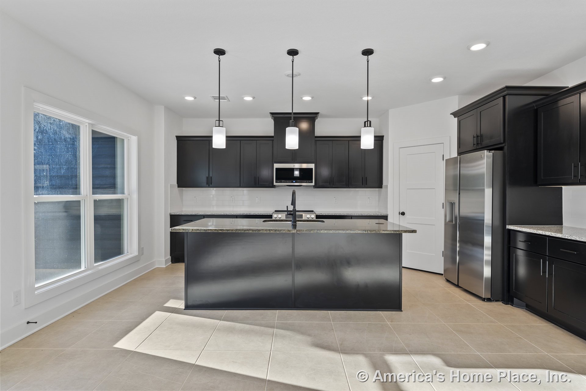 Black shaker cabinets with stainless appliances, granite island topped with pendant lights, white subway tile backsplash, tile flooring, large double window, recessed ceiling