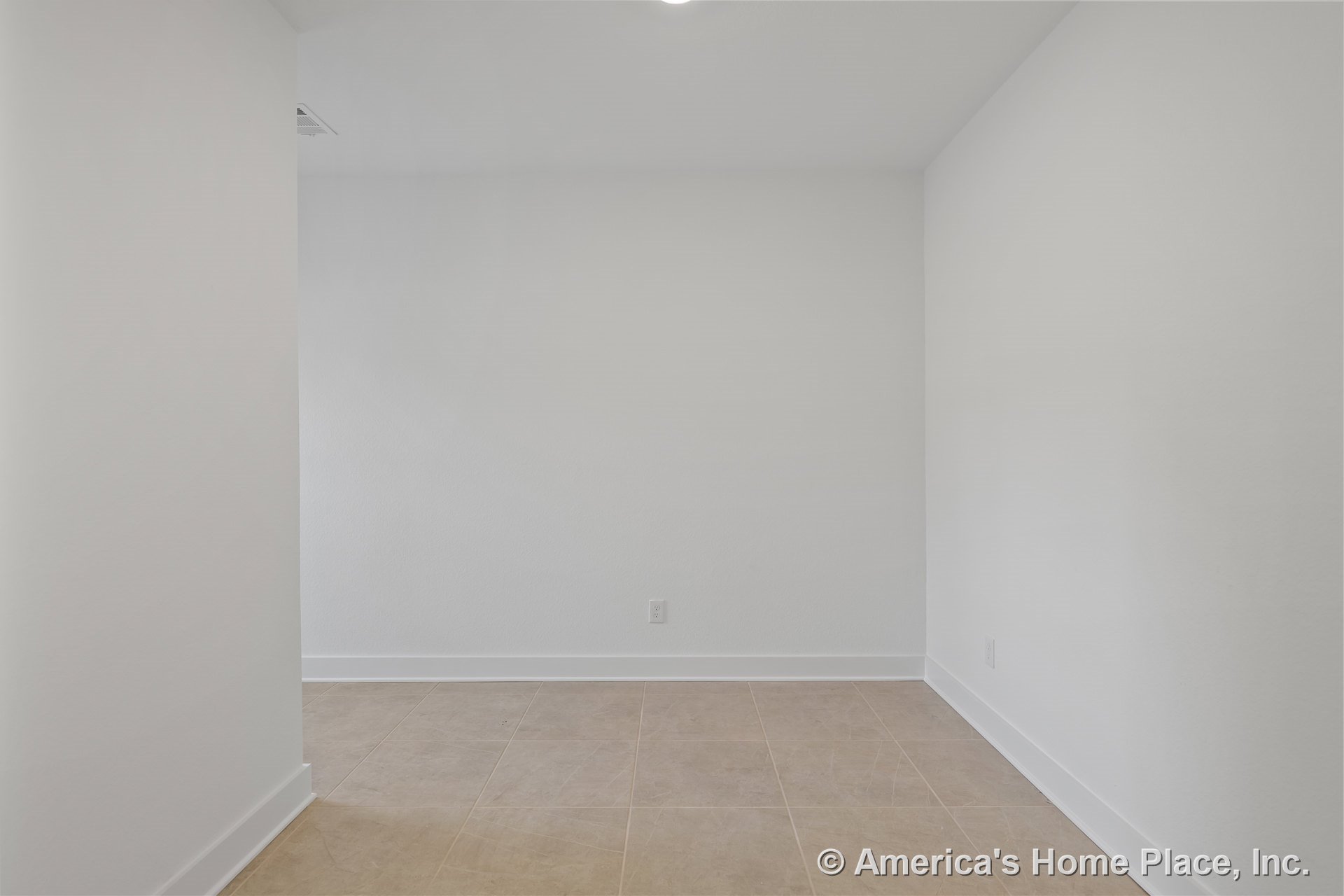 Beige tile flooring, white painted walls with baseboard trim, recessed ceiling light, electrical outlet, minimalist interior corner space with neutral finishes and no windows or