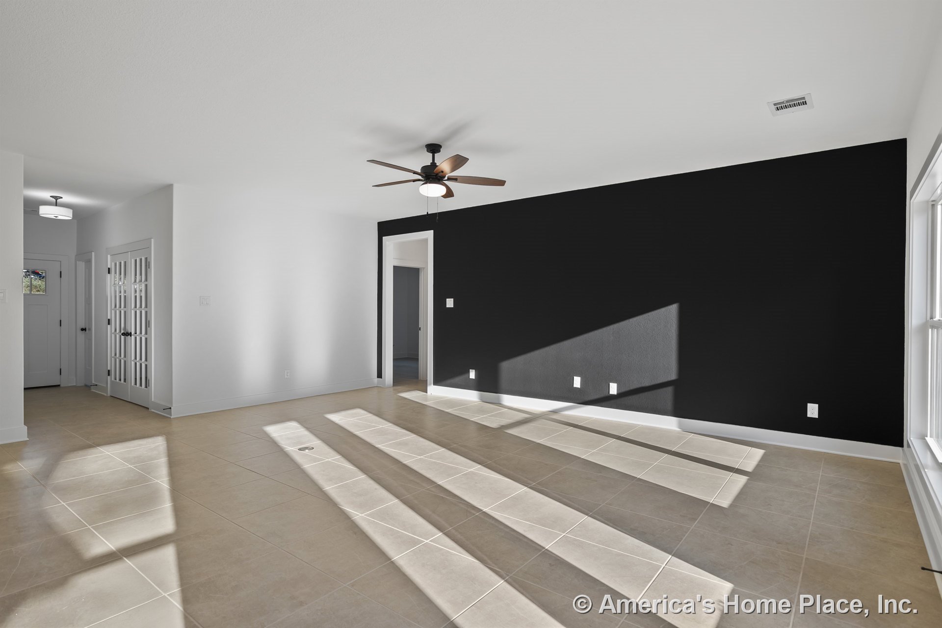 Beige tile flooring, black accent wall, ceiling fan with built-in lighting, white trim and baseboards, double glass doors, and large windows in a modern living room with neutral