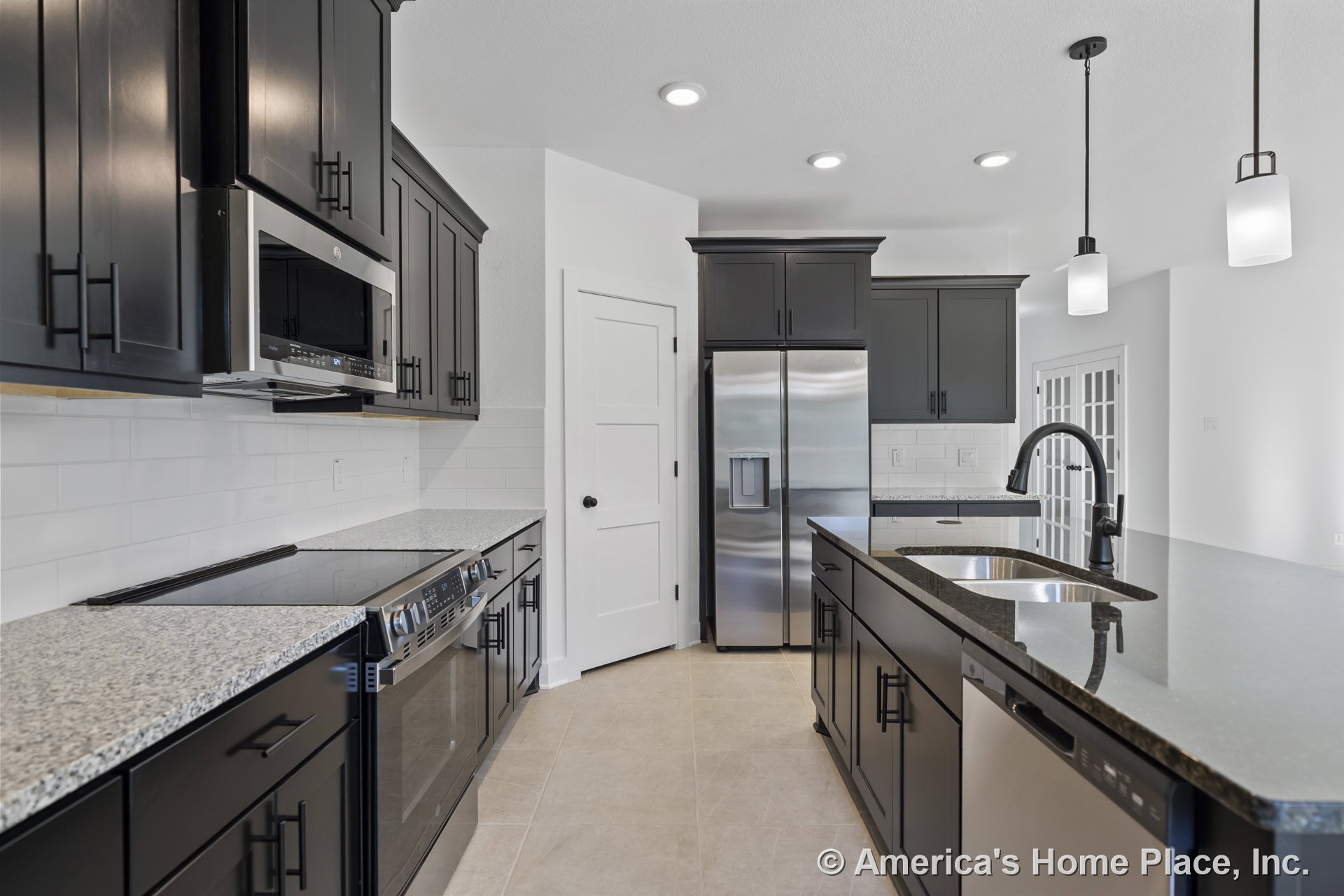 Dark shaker cabinets with granite countertops, stainless steel refrigerator and built-in microwave, tile flooring, undermount sink with modern faucet, and pendant lights above the