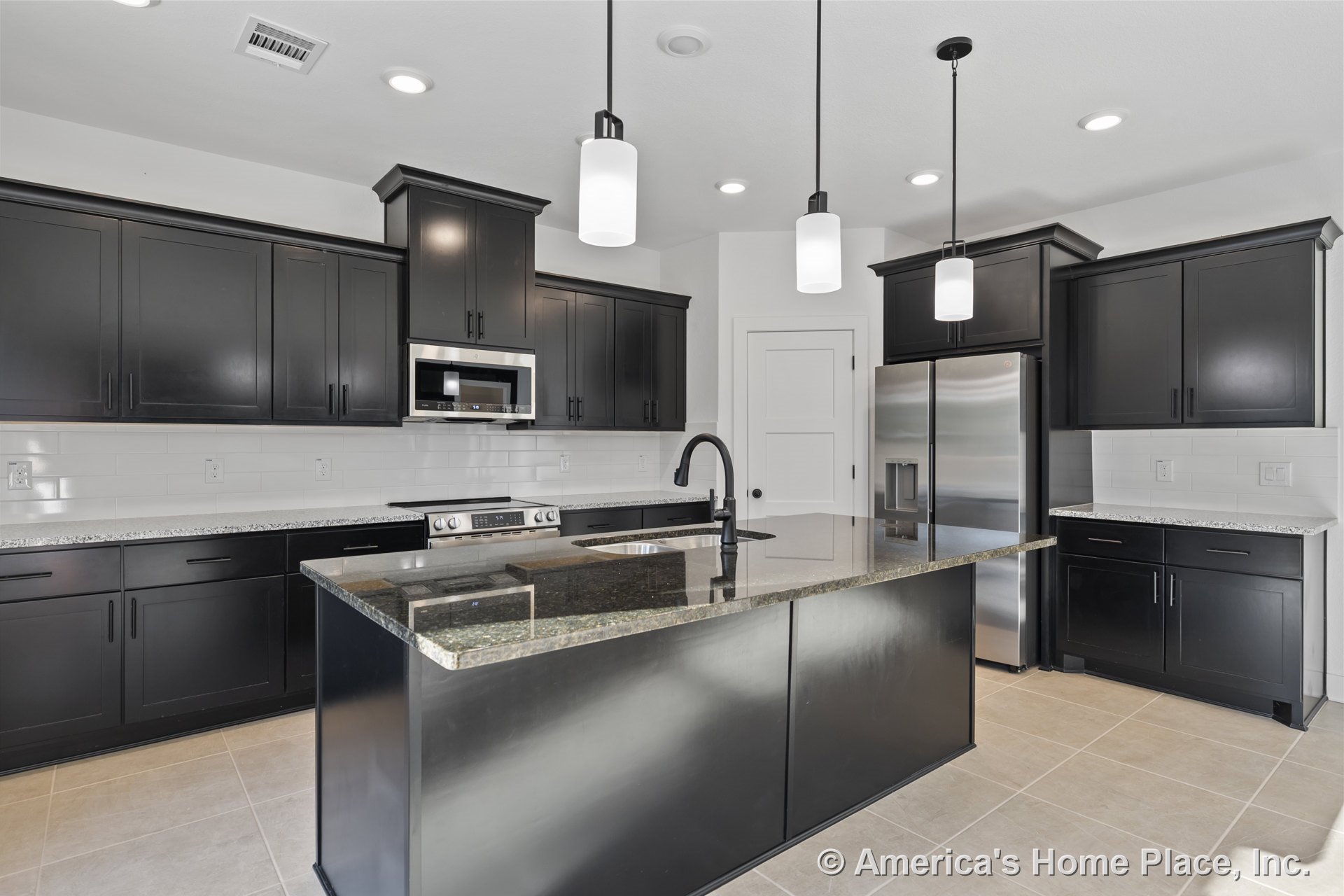 Dark wood kitchen cabinets with granite central island countertop, stainless steel appliances including refrigerator and built-in microwave, white subway tile backsplash, pendant