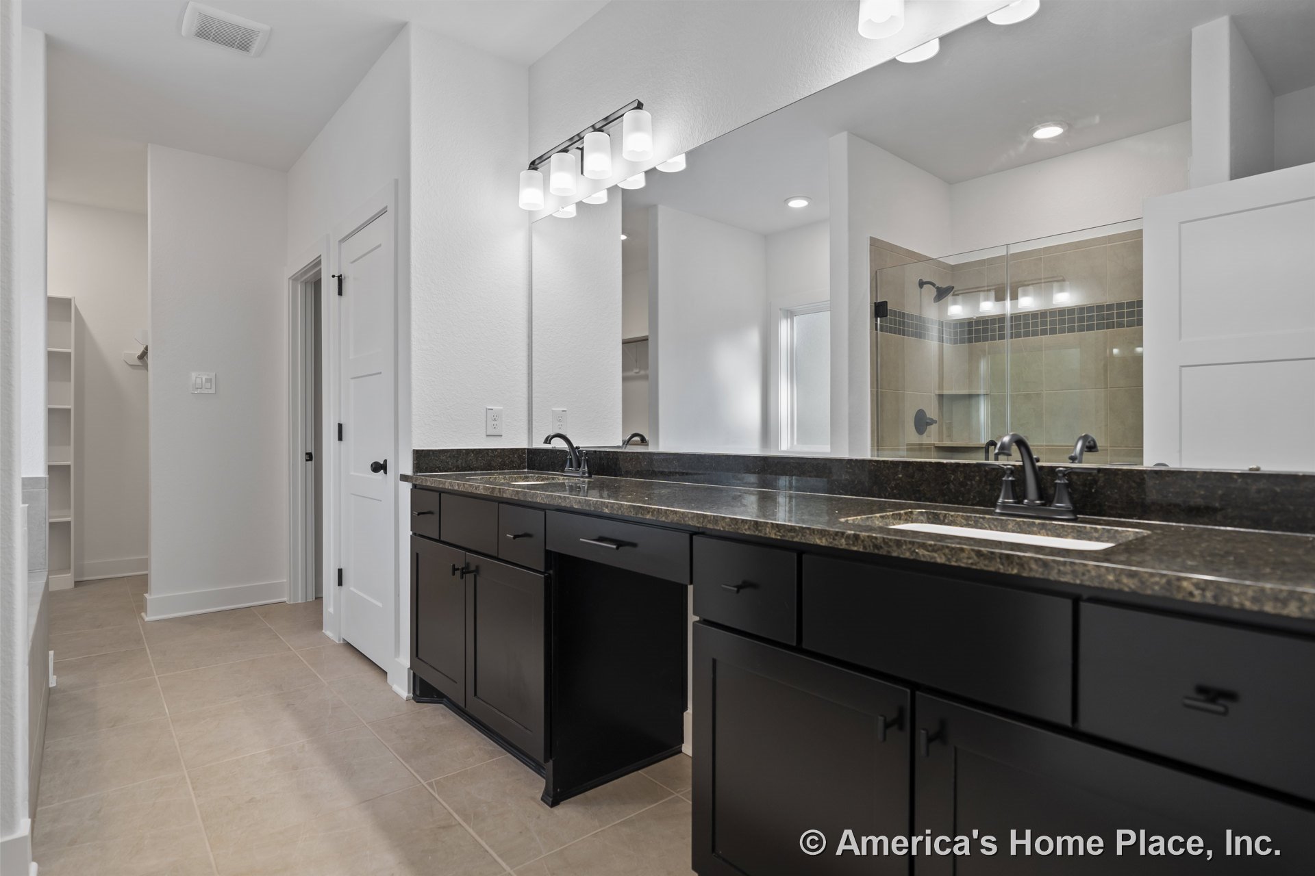 Double vanity with dark wood cabinets and granite countertop, large wall mirror above, glass shower enclosure with modern fixtures, recessed ceiling lights, tile flooring, white