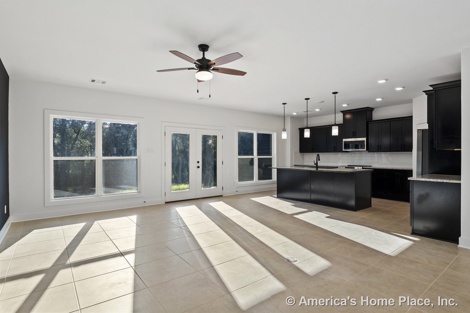 Open concept kitchen and living area with large tile flooring, black cabinetry, granite countertops, pendant and recessed lighting, expansive windows, ceiling fan, double doors