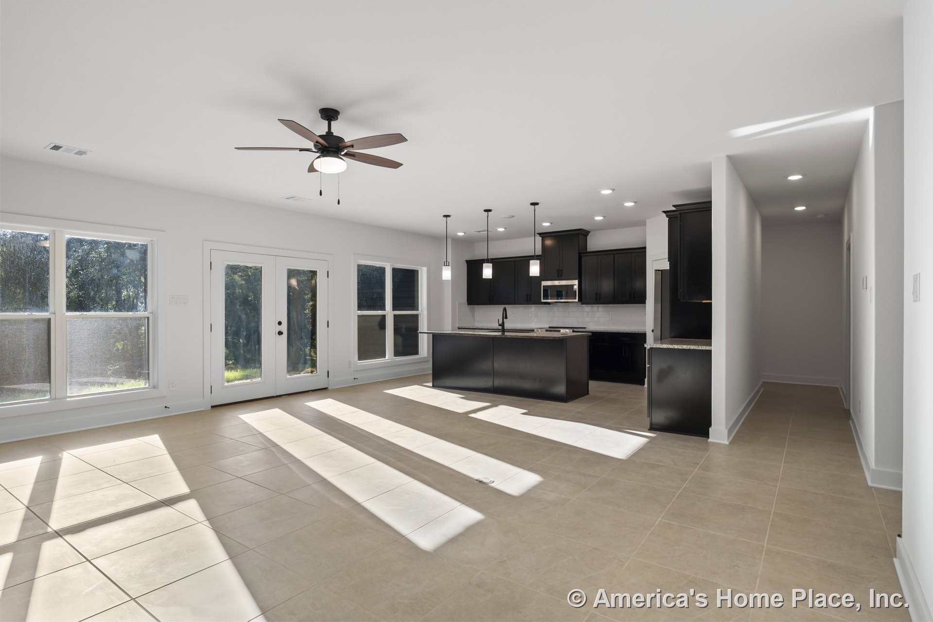 Open-concept living area with large tile flooring, black kitchen cabinetry, granite countertops, pendant lights above the kitchen island, ceiling fan with light, recessed lighting