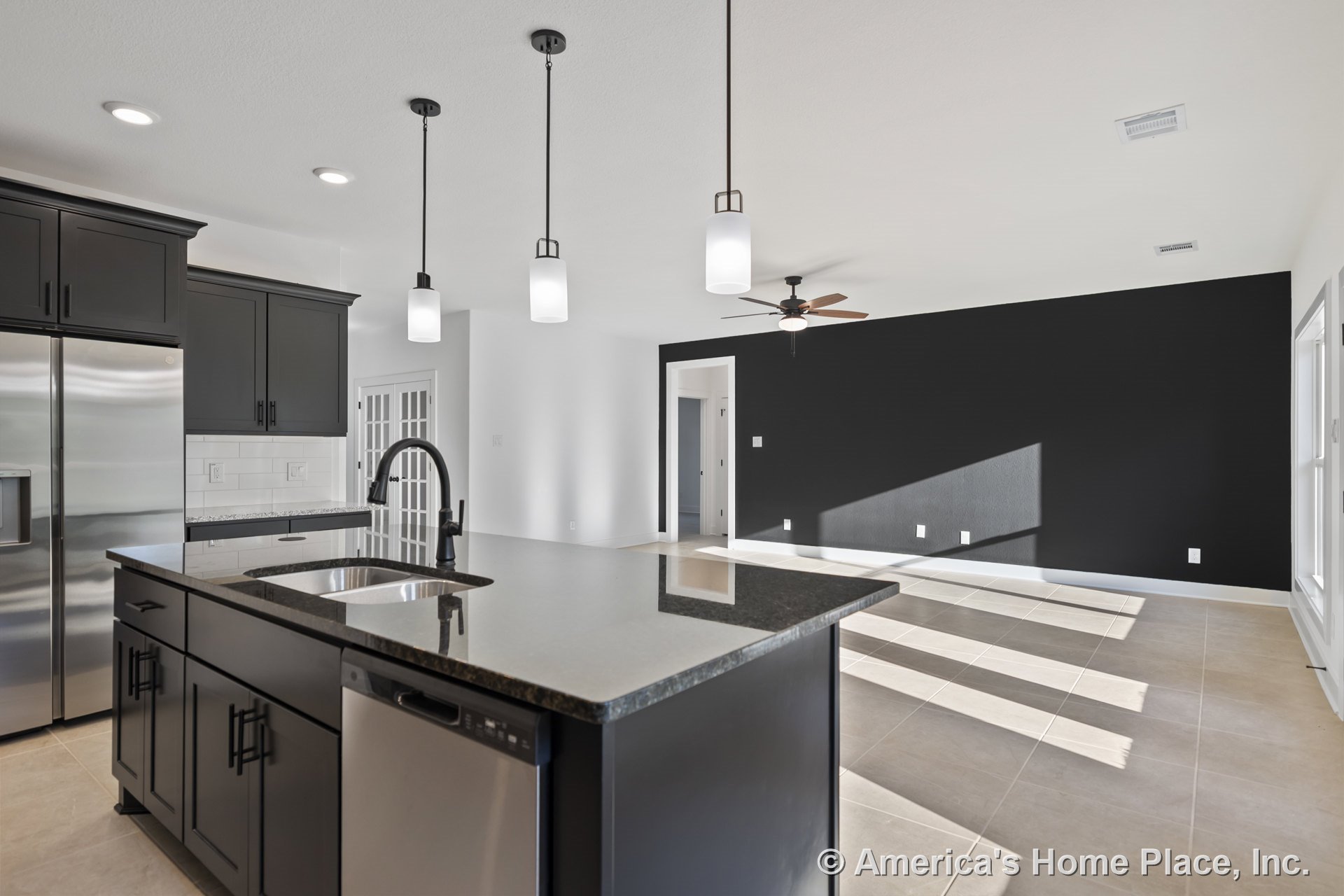 Black kitchen cabinetry with granite countertops and stainless steel appliances, large kitchen island, pendant and recessed lighting, tile flooring throughout, open floor plan