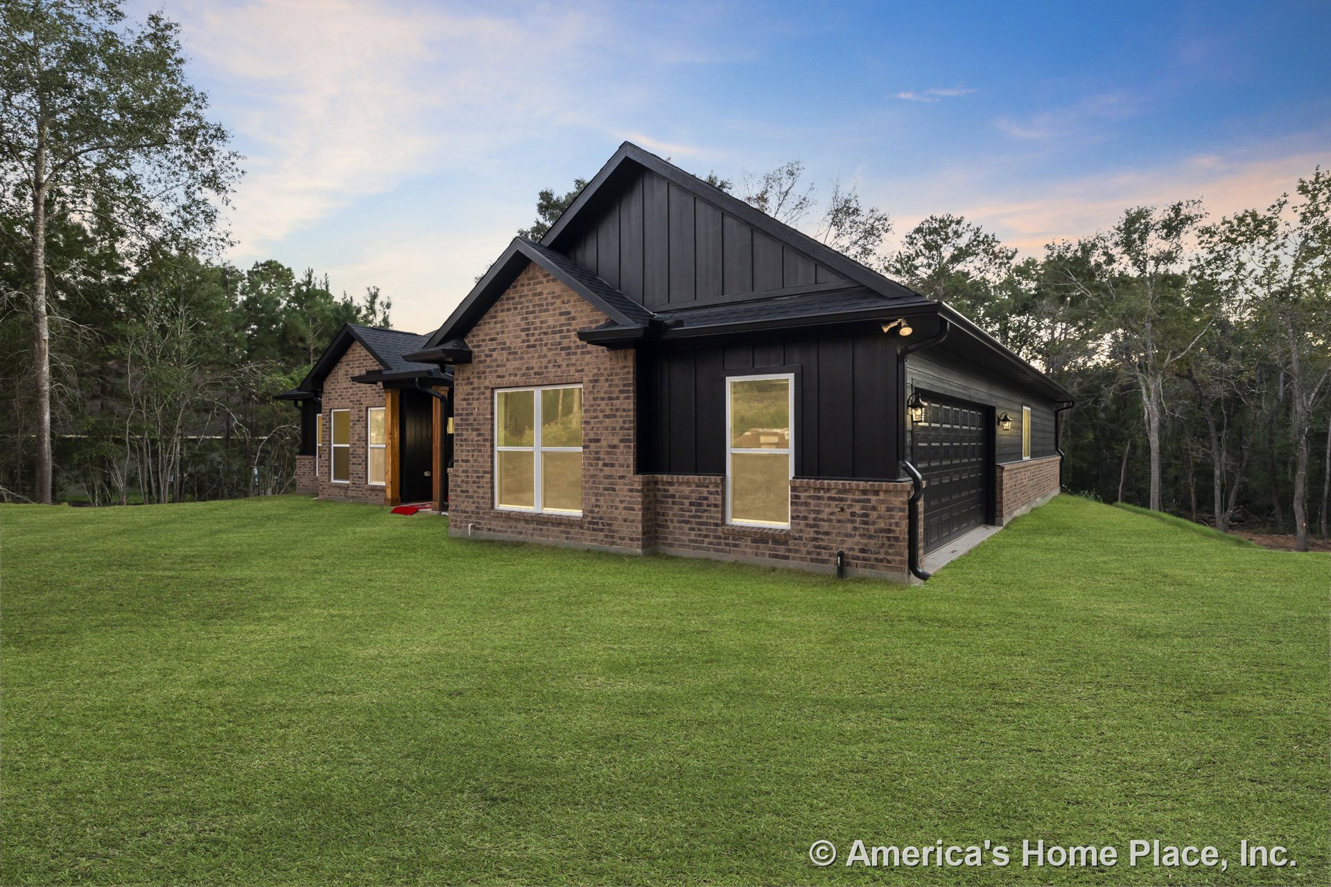 Brick facade with black vertical siding, attached two-car garage, multiple large windows, gabled roof, outdoor lighting fixtures, and contrasting trim at front entry.