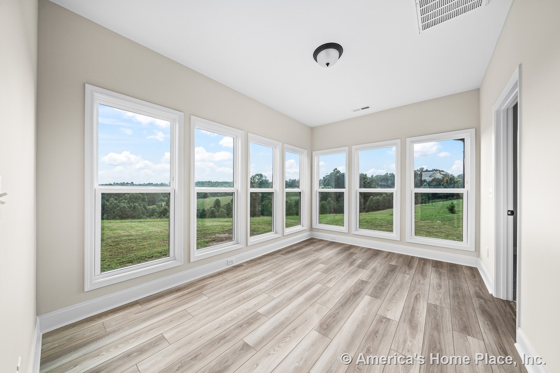 Sunroom with six tall windows, light wood plank flooring, white window trim and baseboards, neutral wall paint, and a flush mount ceiling light.