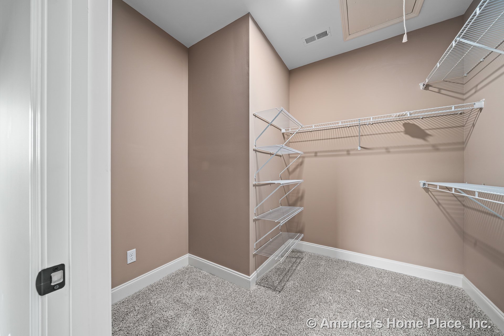 Walk-in closet with built-in wire shelving units, beige painted walls, carpet flooring, white baseboards, ceiling attic access panel, and ceiling vent.
